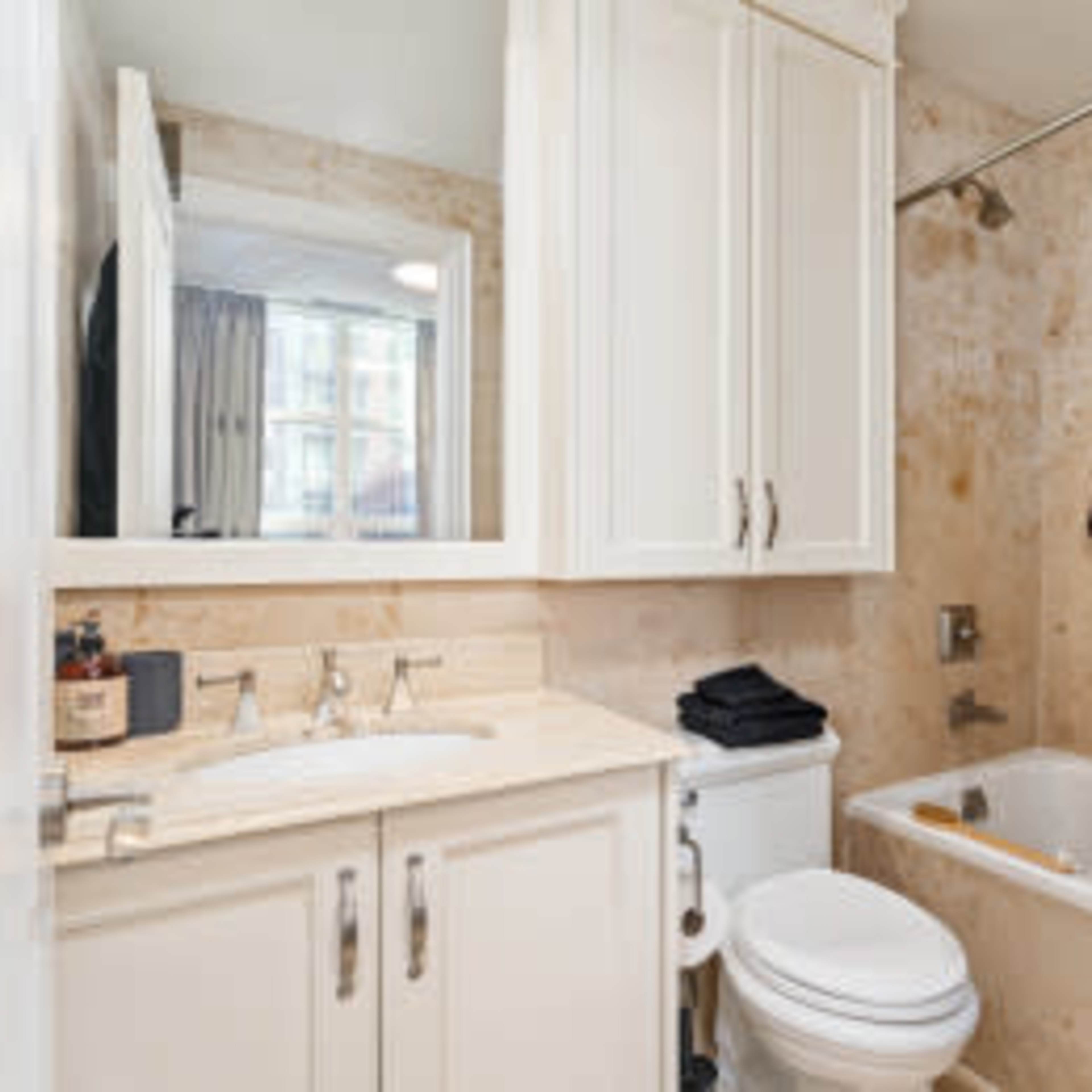 A small bathroom featuring a bathtub with a shower curtain, a sink with cabinets, and a toilet.