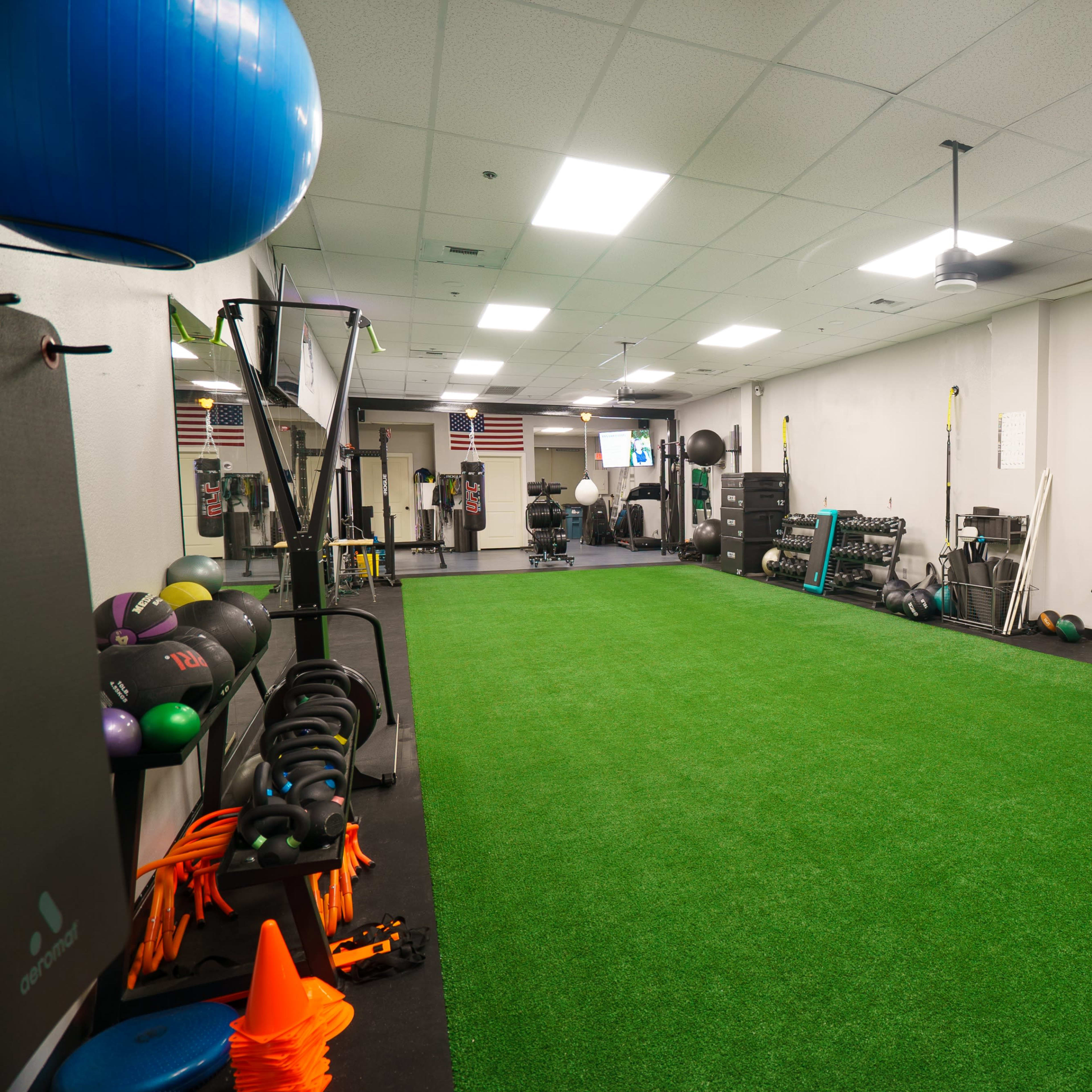 A spacious gym area featuring artificial turf, various fitness equipment, and exercise accessories along the walls.