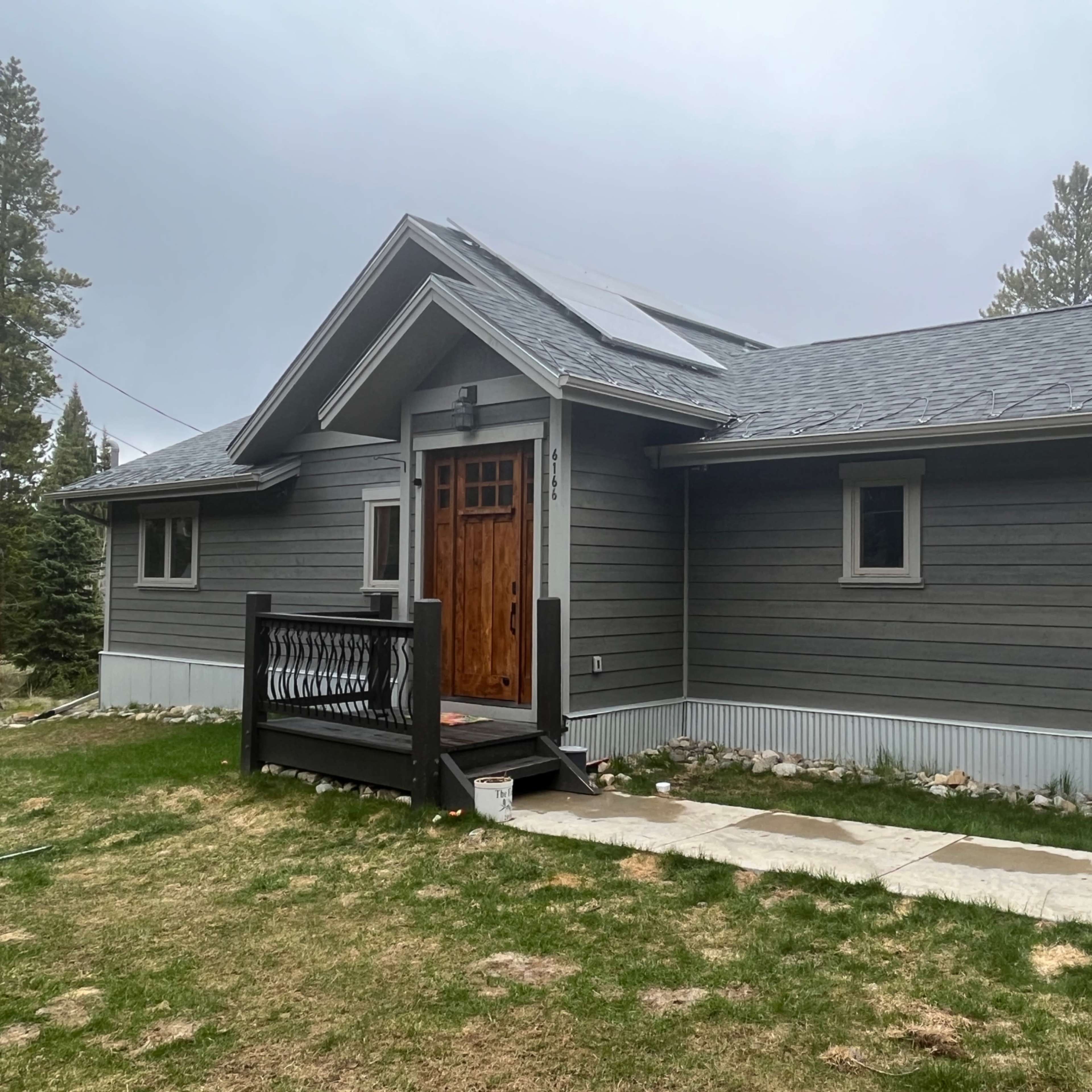 A modern gray wooden house with a sloped roof, featuring a wooden front door and a small porch.