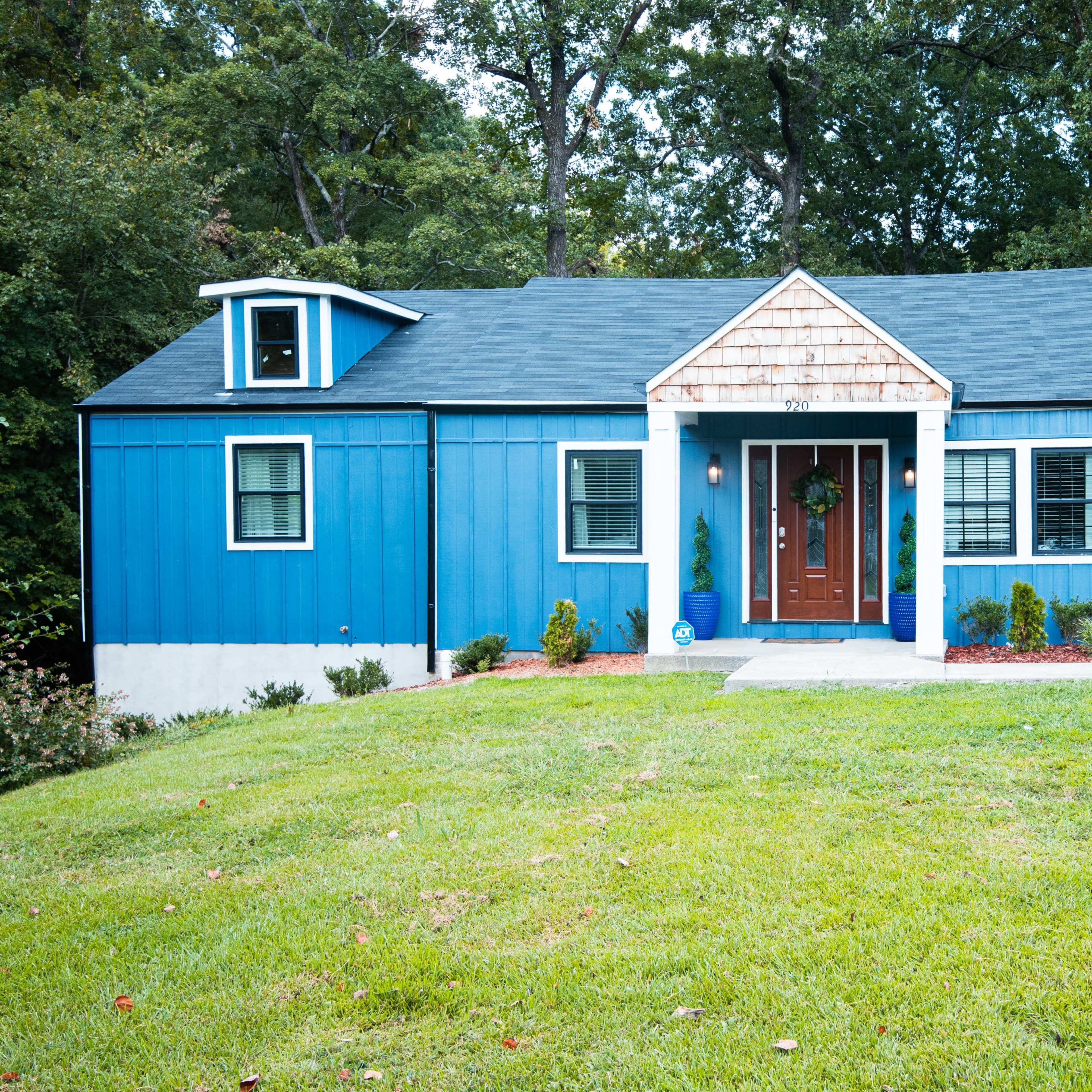 A blue, single-story house with a symmetrical design features a central entrance and two small dormers on the roof.