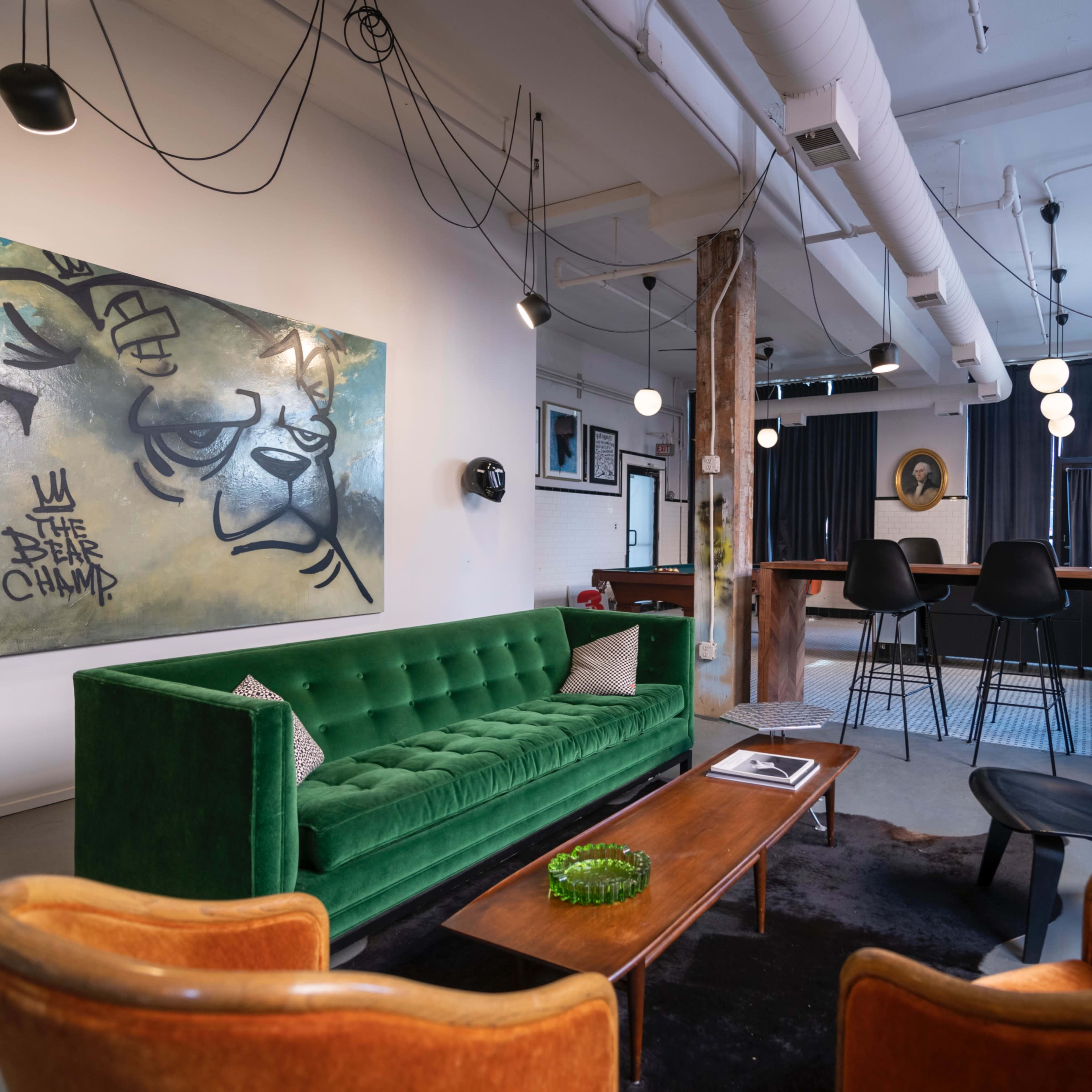 A stylish interior featuring a green velvet sofa, a wooden coffee table, and a bar area with high chairs, complemented by a large wall art piece.