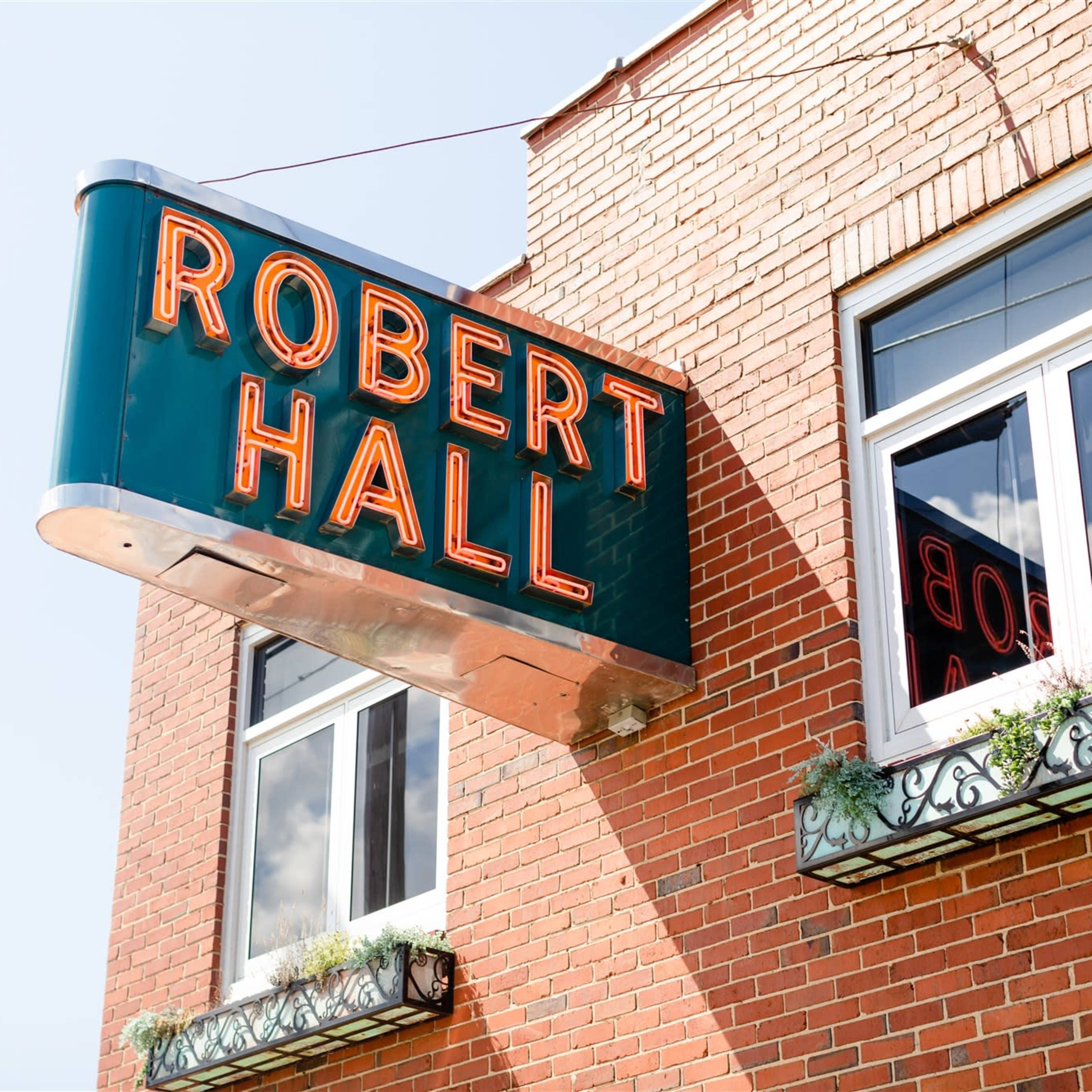 A neon sign reading "ROBERT HALL" is mounted above a brick building with windows and decorative planters.