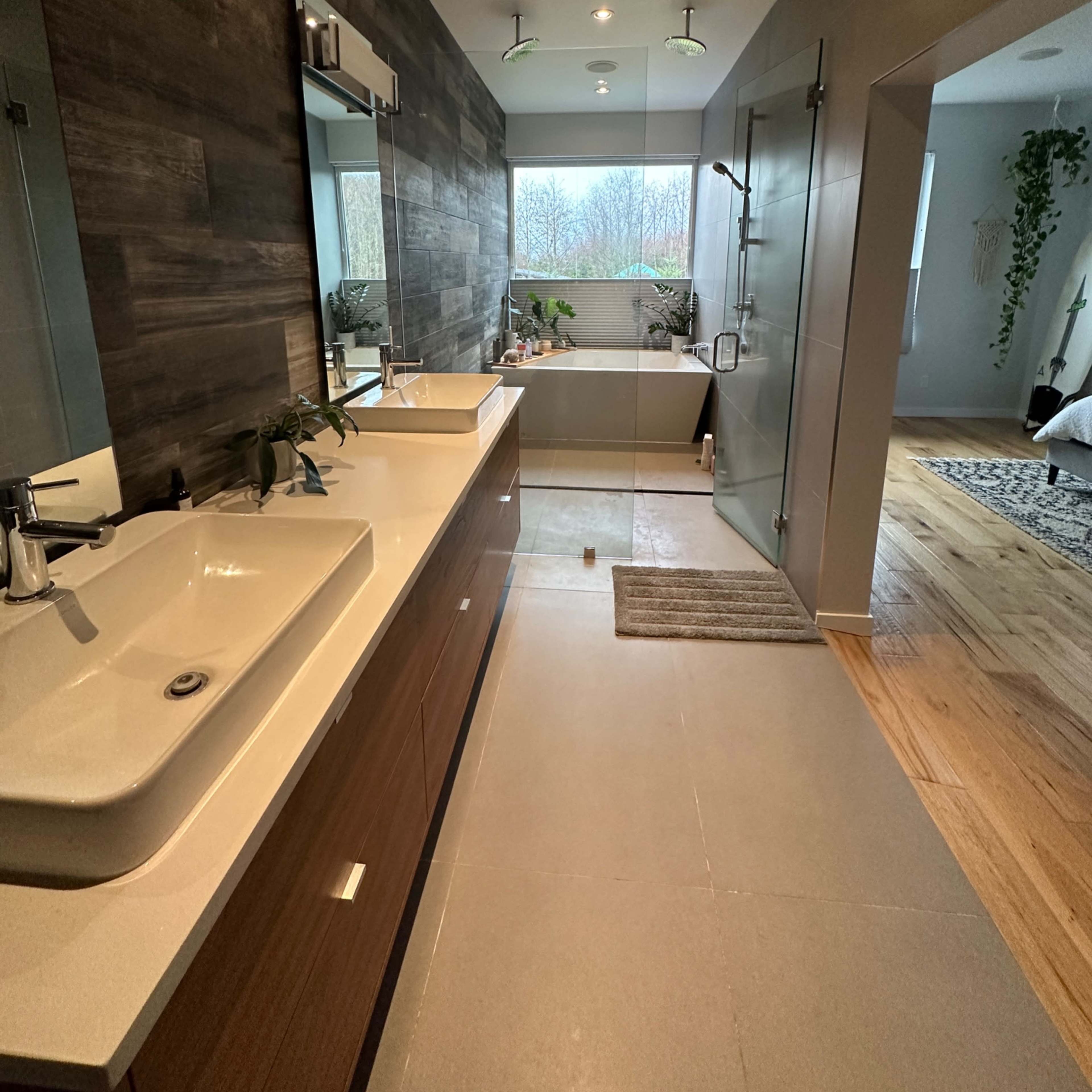 A modern bathroom with a double vanity, large windows providing natural light, and a glass shower enclosure.