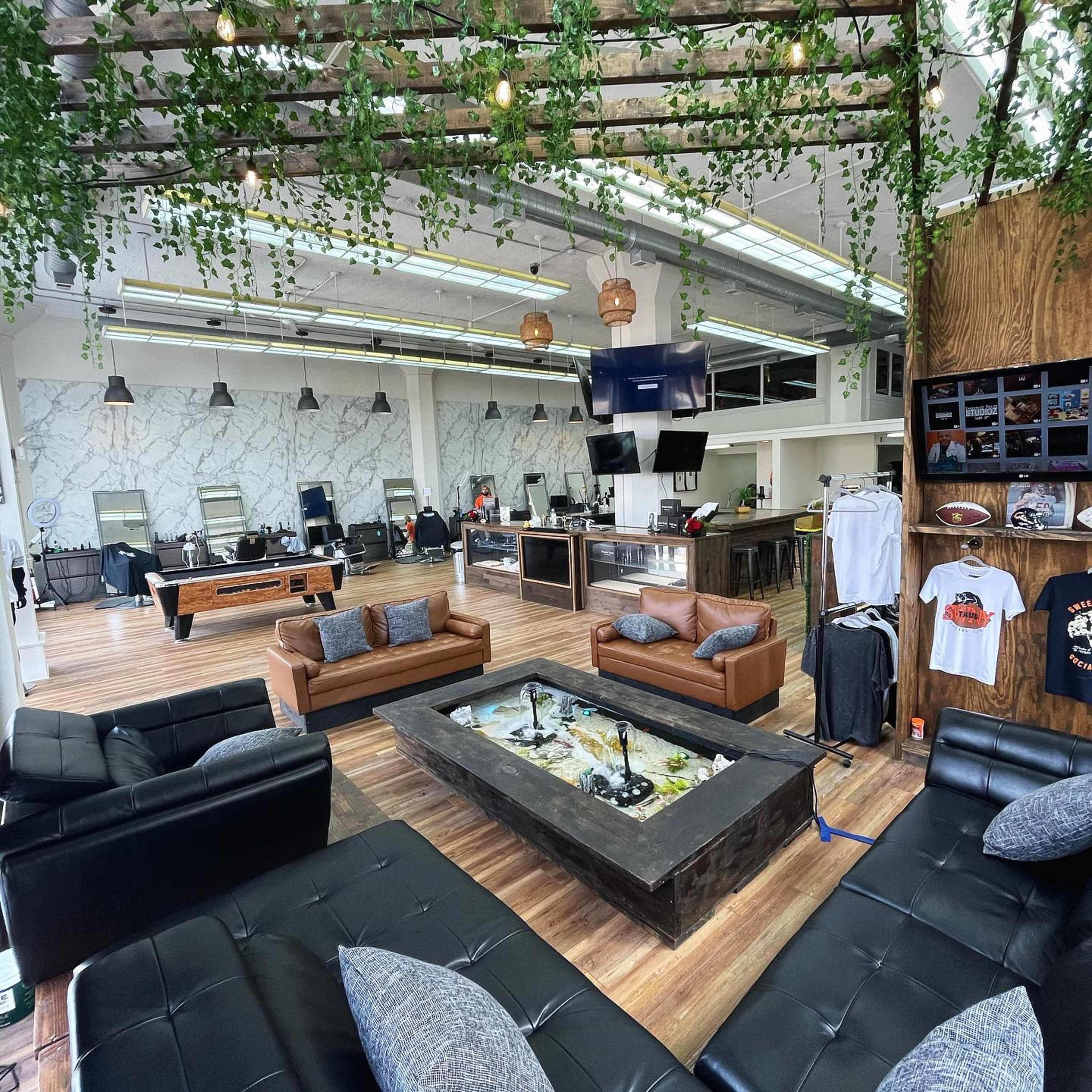 A stylish lounge area featuring leather sofas, a central table with plants, and a pool table, all within a spacious room with marble walls and modern decor.