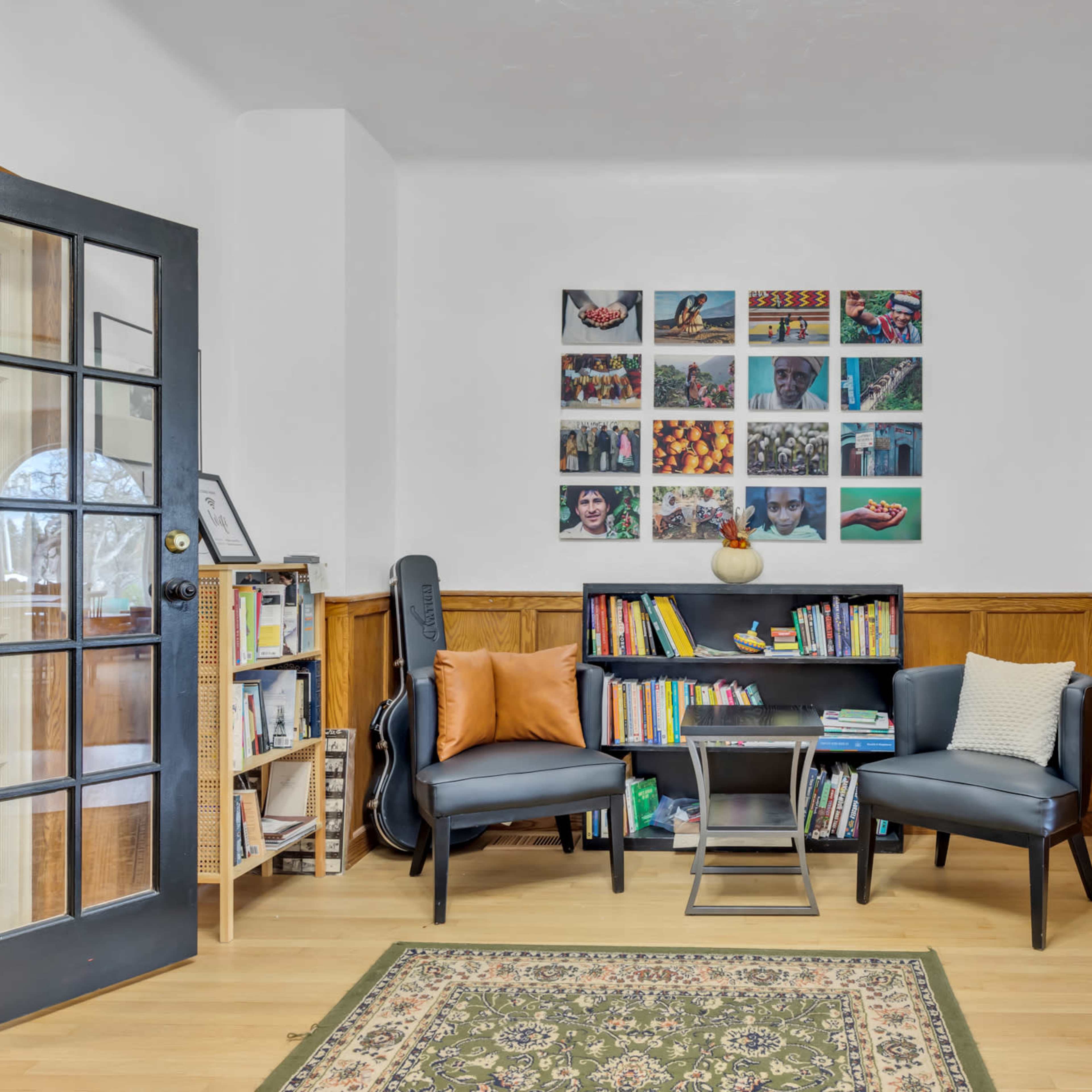 A cozy reading corner features two chairs, a small bookshelf filled with books, and a colorful wall display of photographs.
