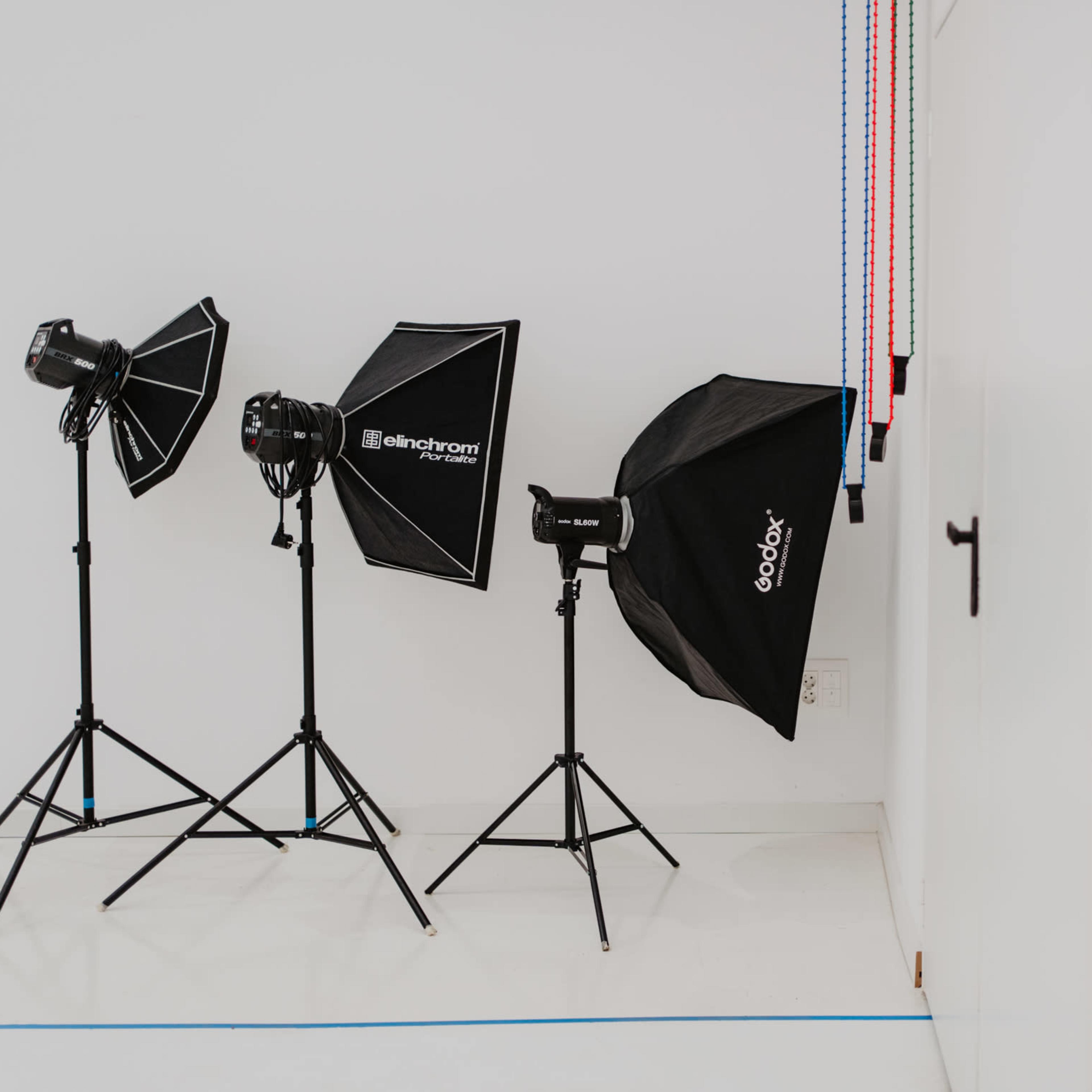 Three lighting setups on stands in a studio with a plain white wall and a closed door.