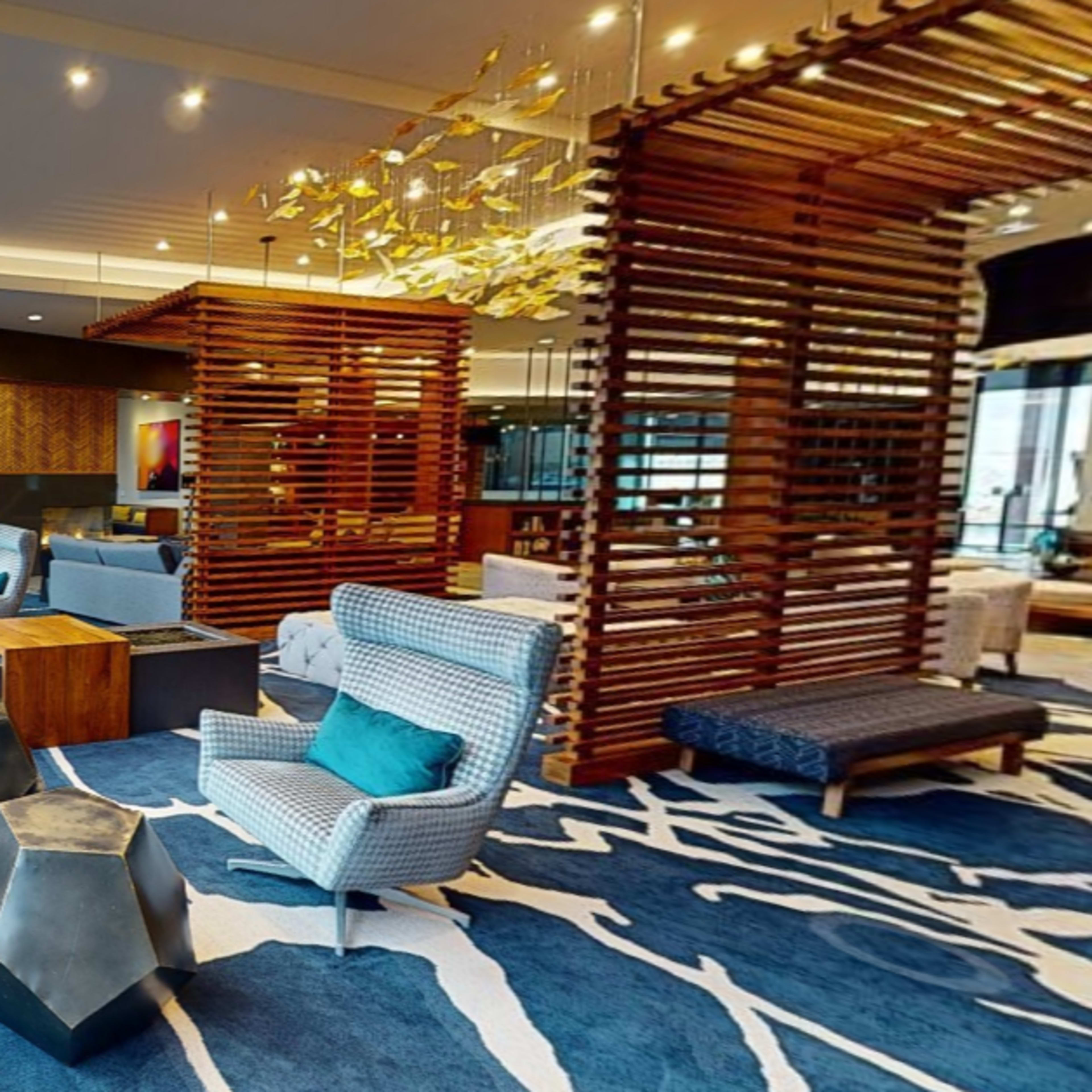 A modern lobby area with patterned rugs, wooden structures, and a mix of seating arrangements including couches and chairs.