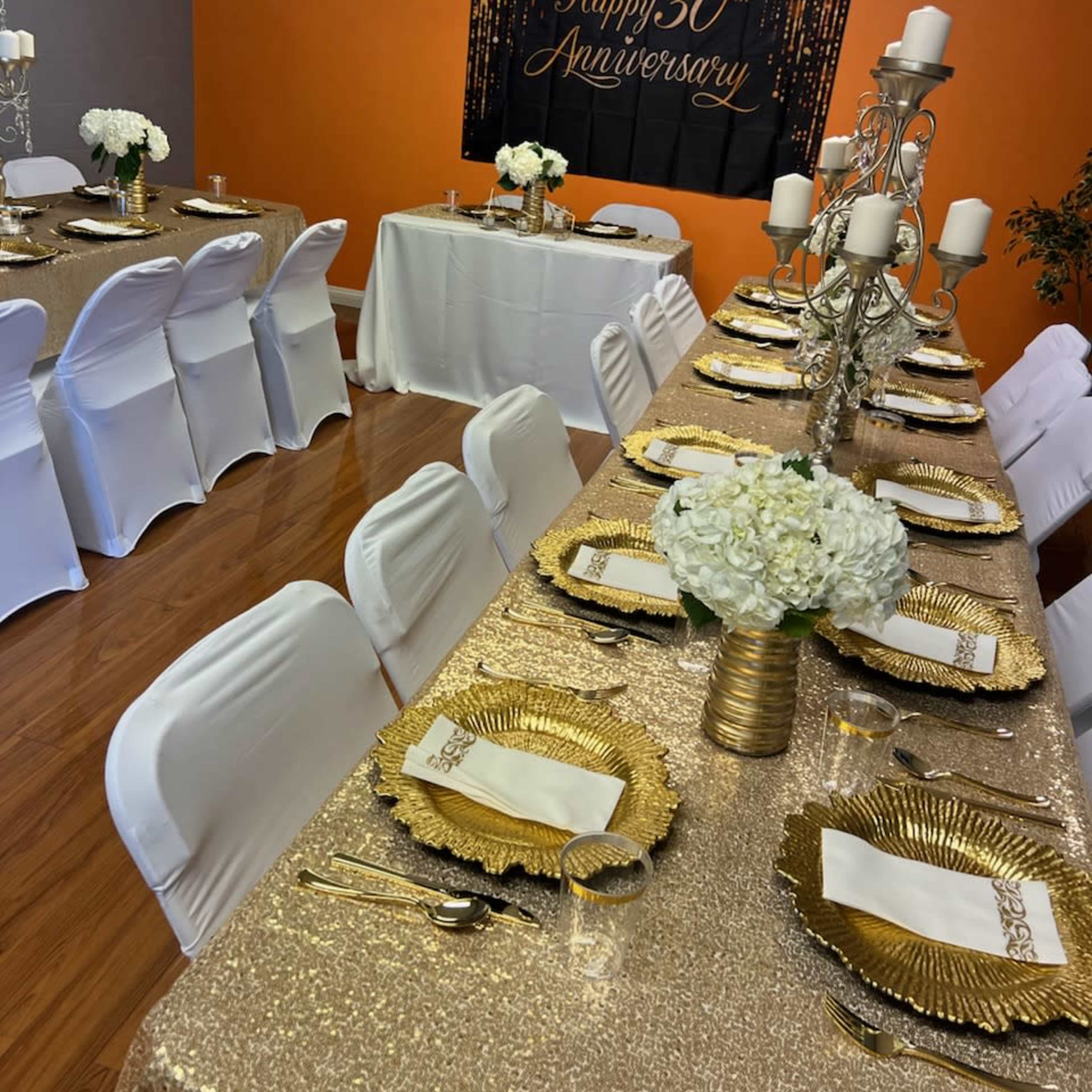 A decorated banquet room with tables covered in gold tablecloths, set with elegant dinnerware, and a backdrop celebrating a 30th anniversary.