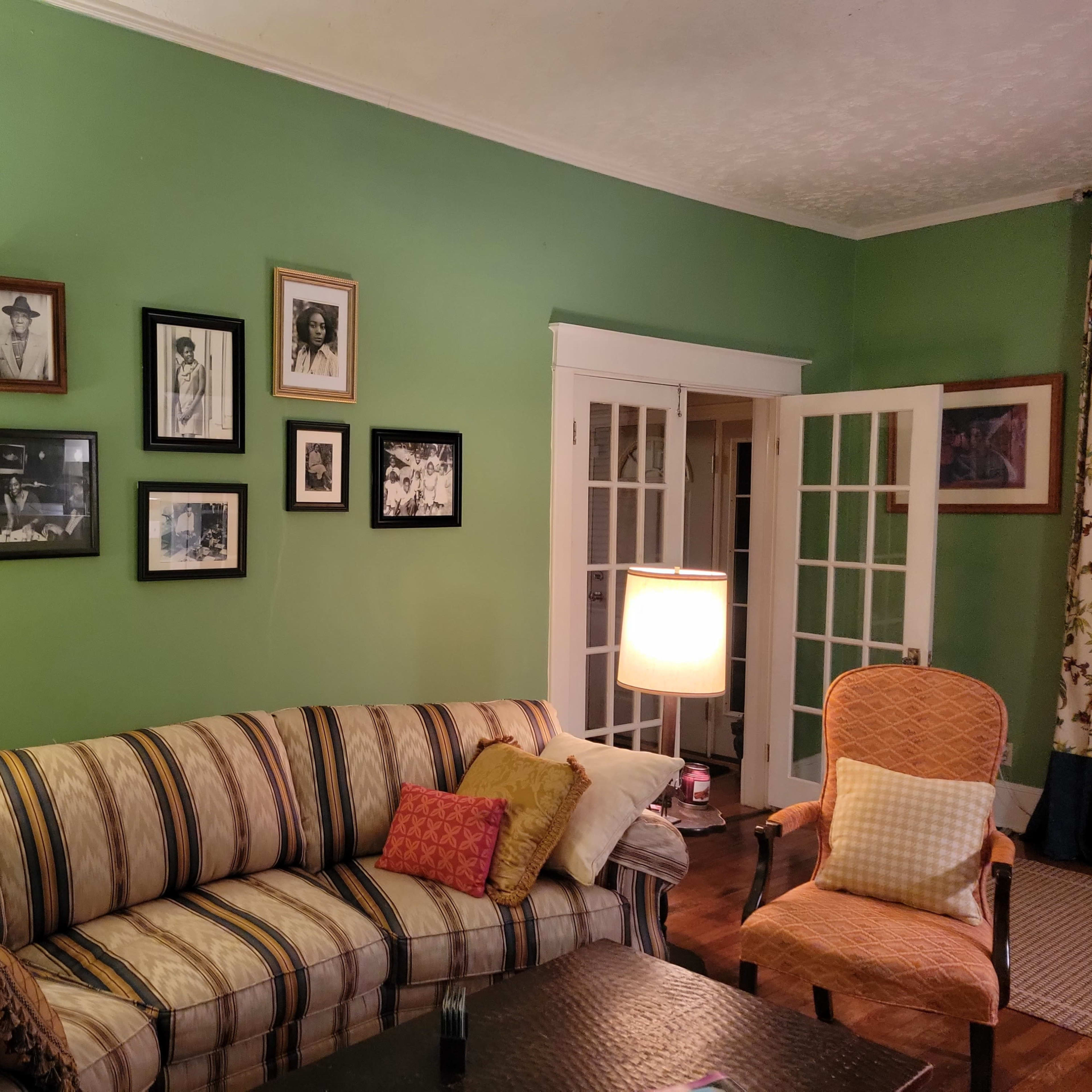 A green living room features a striped sofa, a lamp, and a wall decorated with framed black and white photographs.