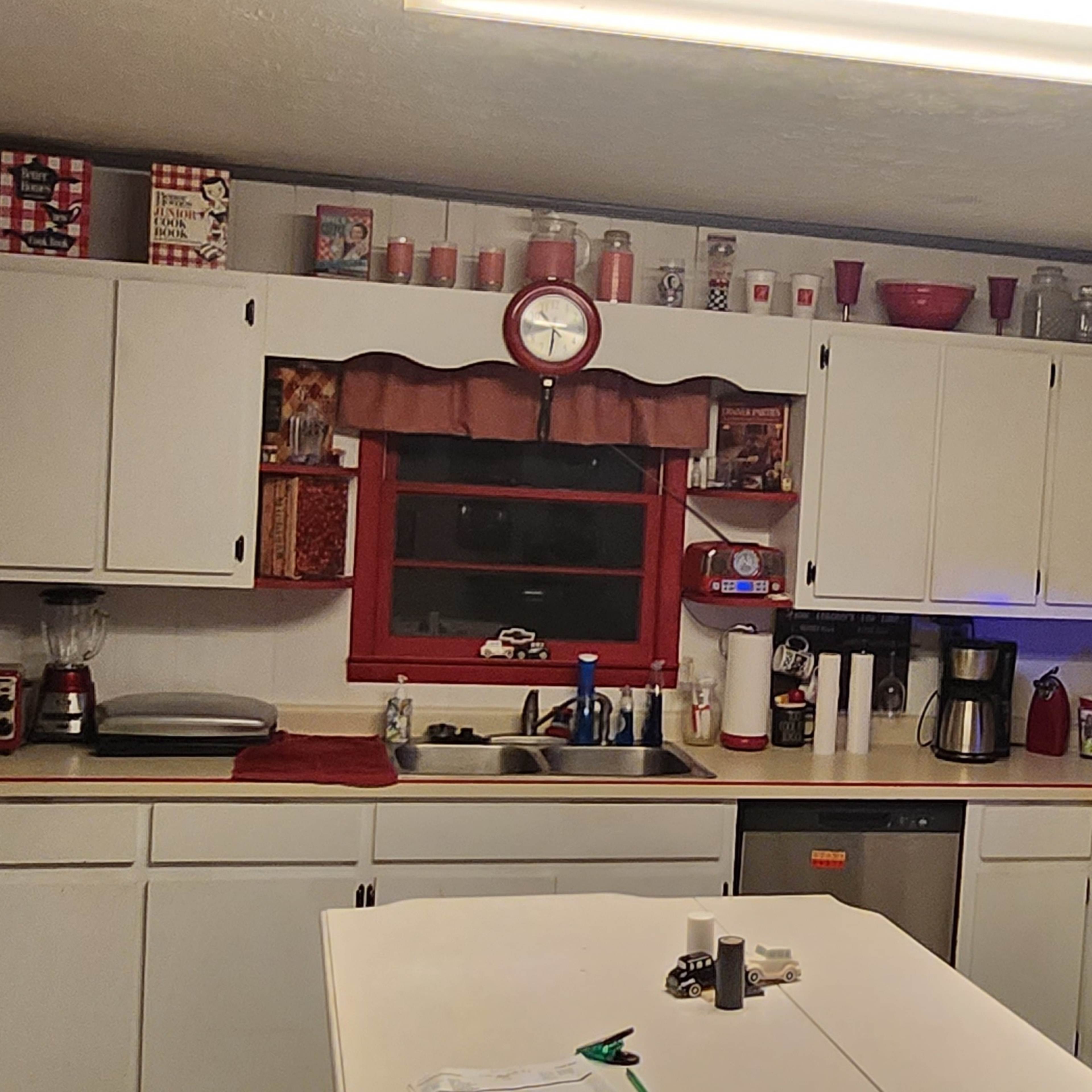 A kitchen features white cabinetry, a central island, and various kitchen appliances with a red and silver color scheme.