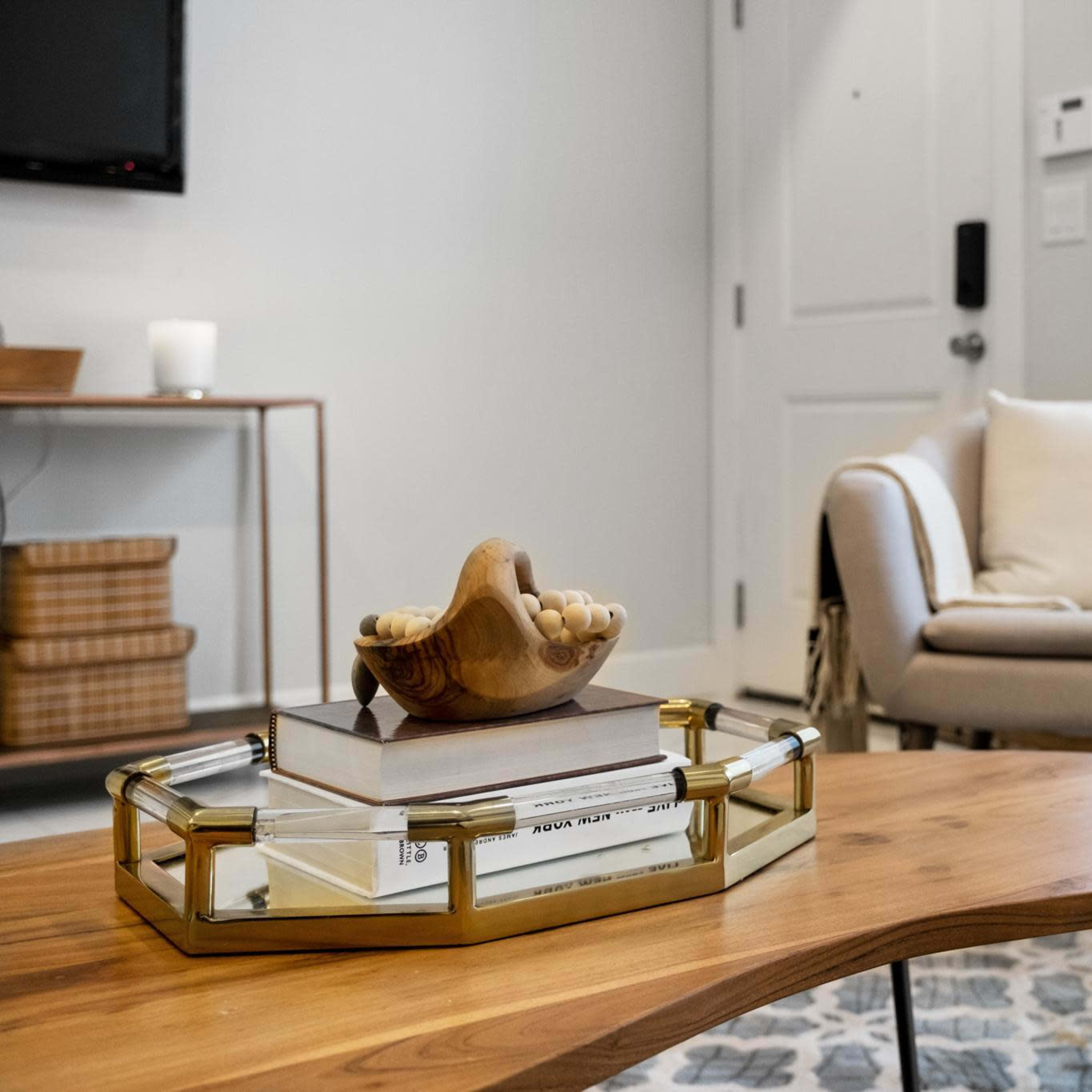 A wooden coffee table with a decorative shell sits in foreground, with a light-colored armchair and a window in the background.
