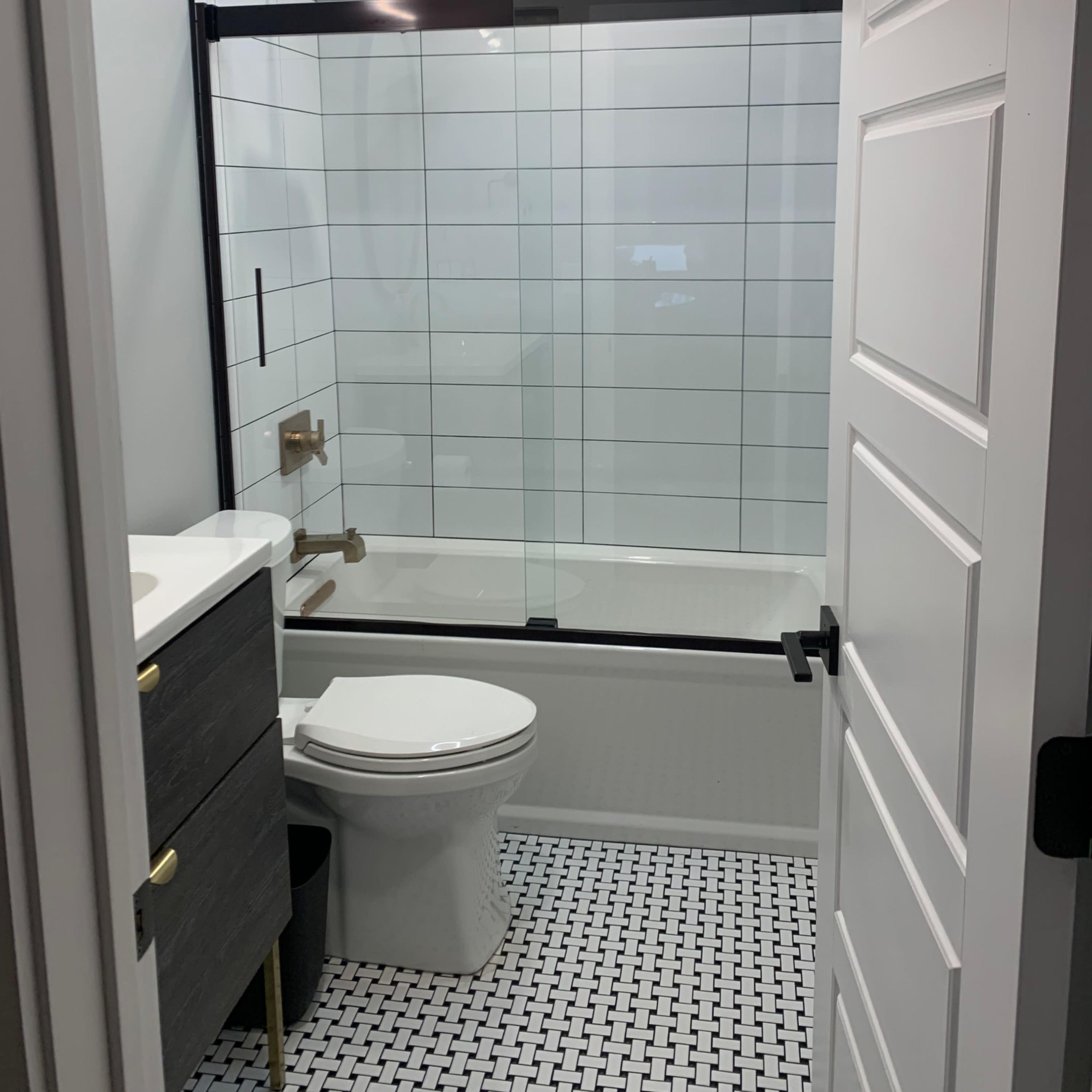 A bathroom with a glass shower enclosure, a toilet, a vanity with a sink, and patterned floor tiles.