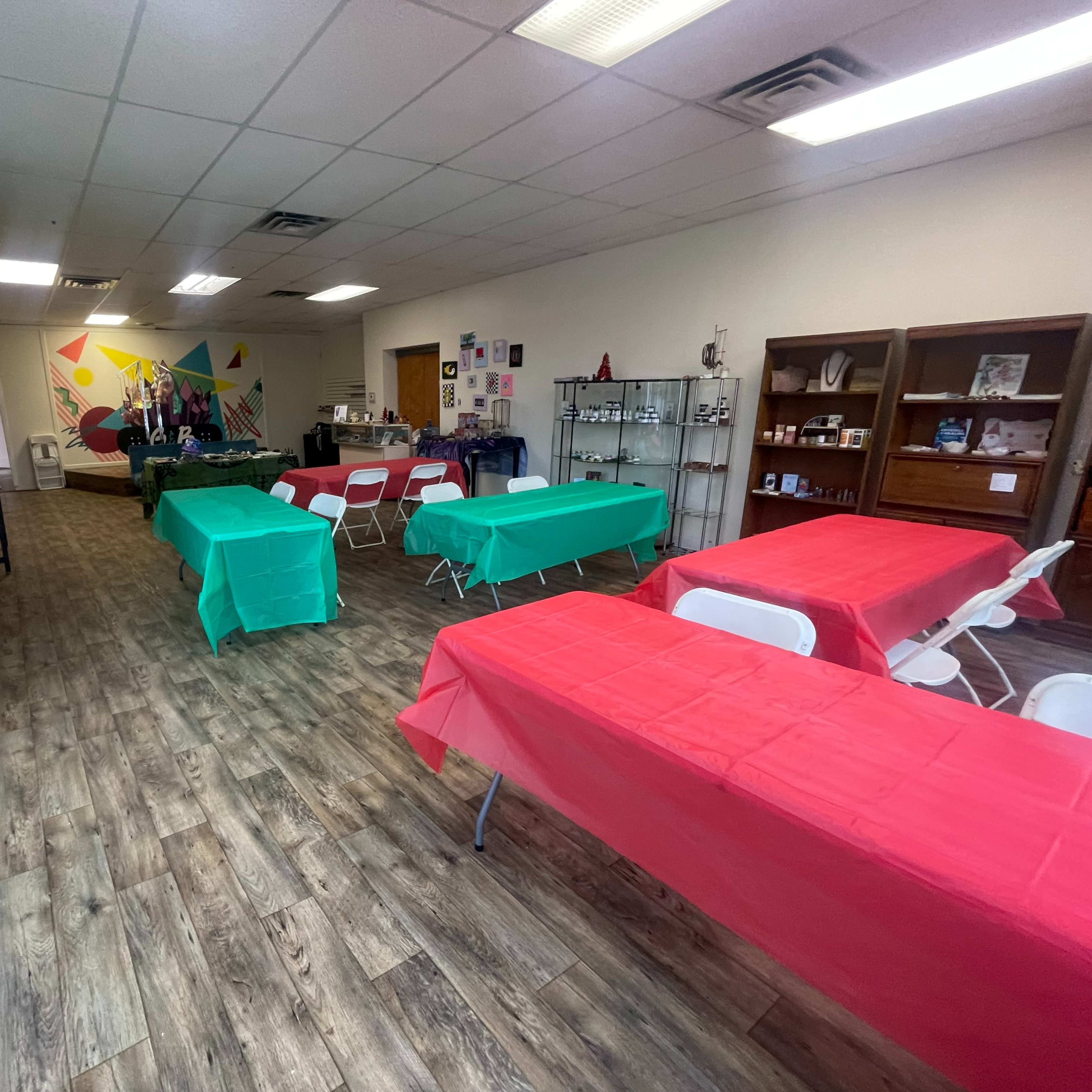 The room features several tables covered in red and green tablecloths, with a coffee station and display shelves in a communal setting.