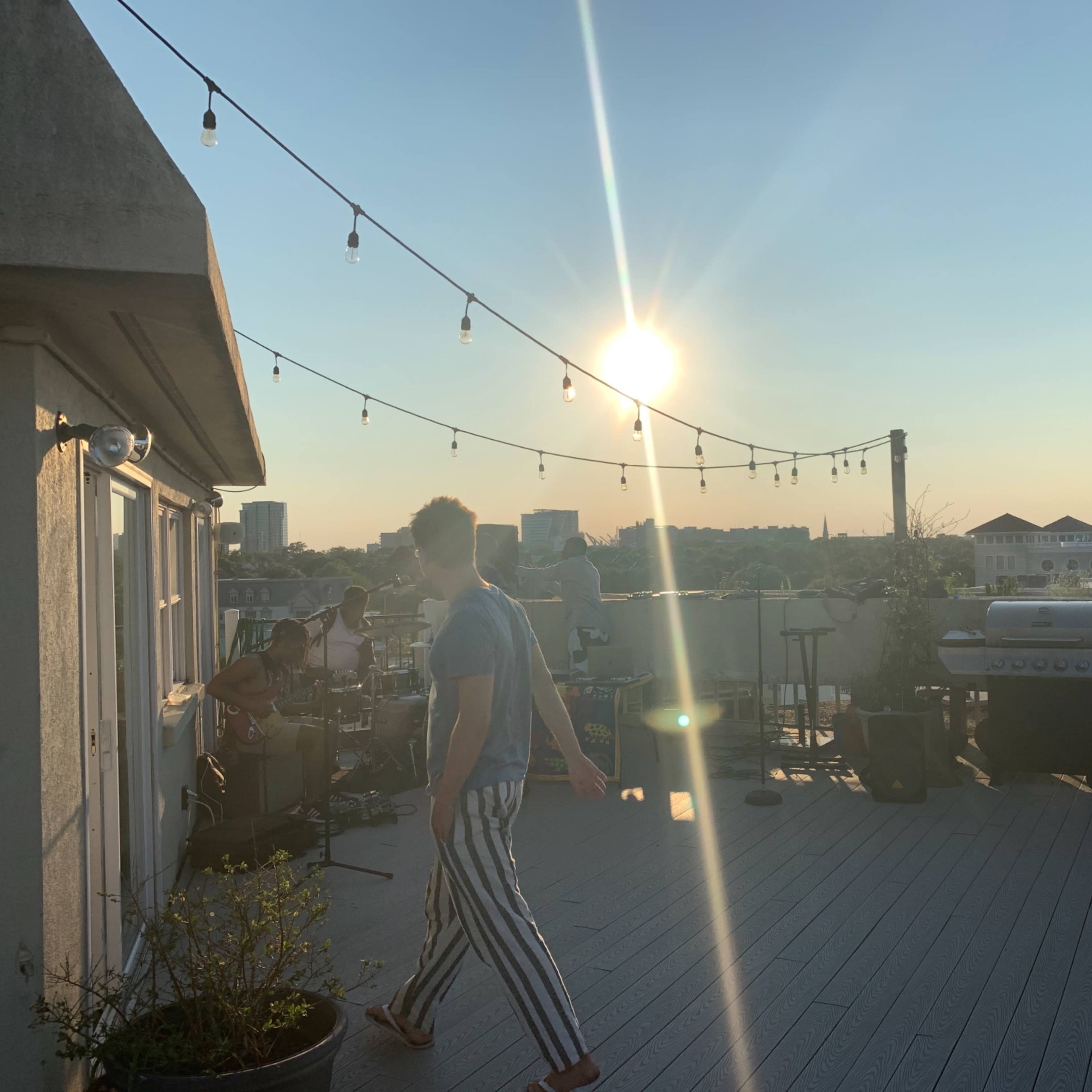 A rooftop gathering features people enjoying music under string lights with a sunset backdrop.