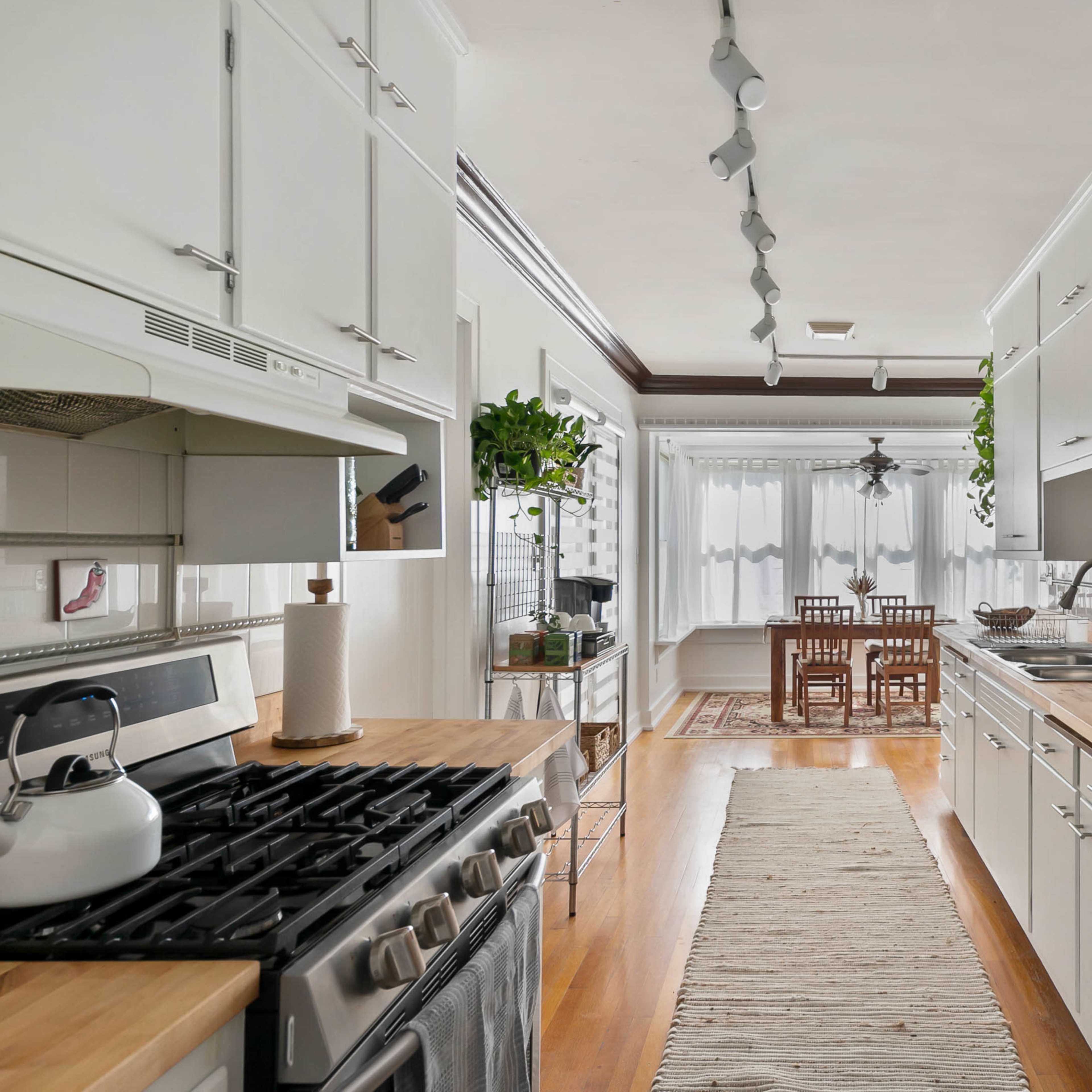 A modern kitchen features stainless steel appliances, wooden countertops, and a dining area with a wooden table and chairs bathed in natural light.