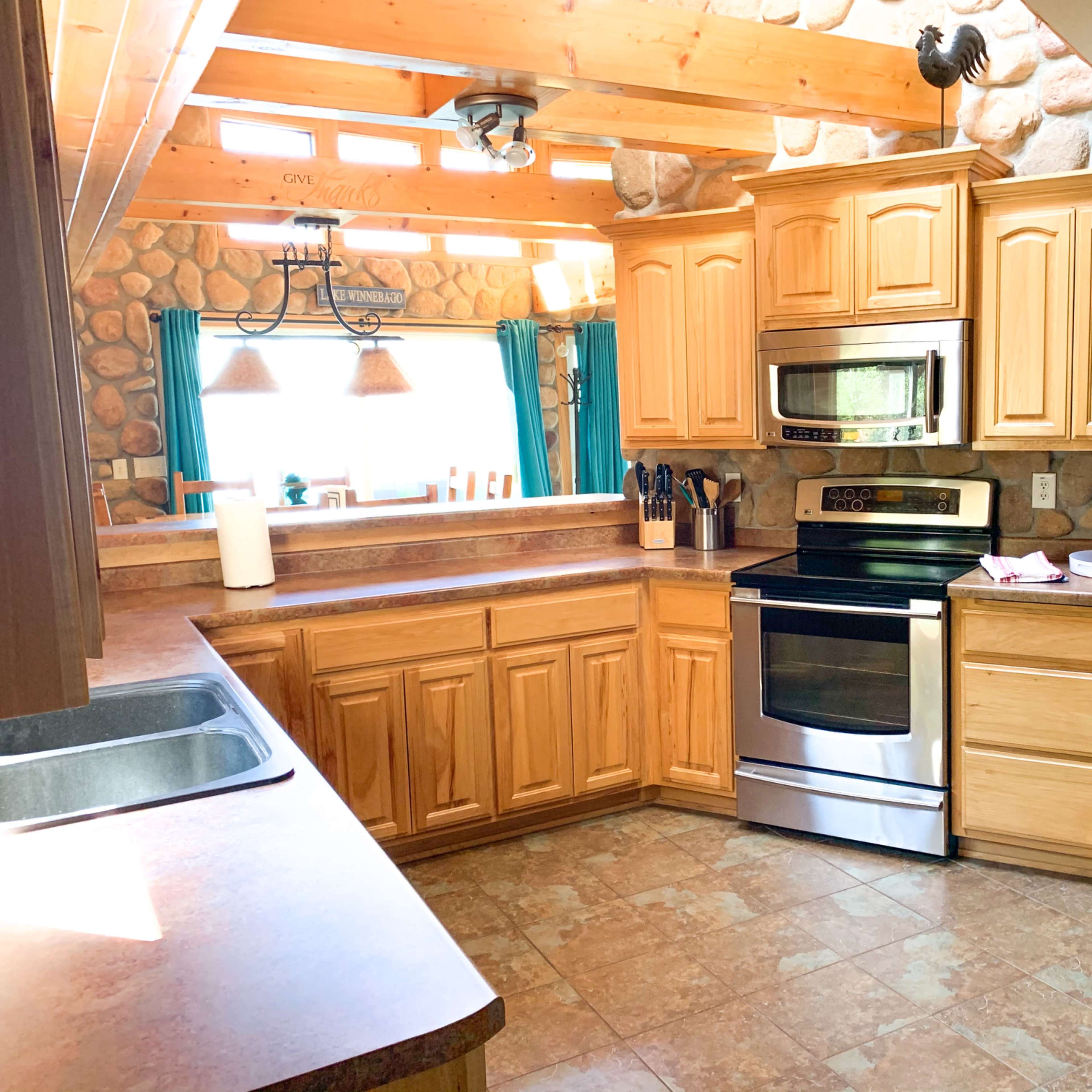 A kitchen with wooden cabinets, a stainless steel stove and microwave, and a stone wall in a rustic setting.