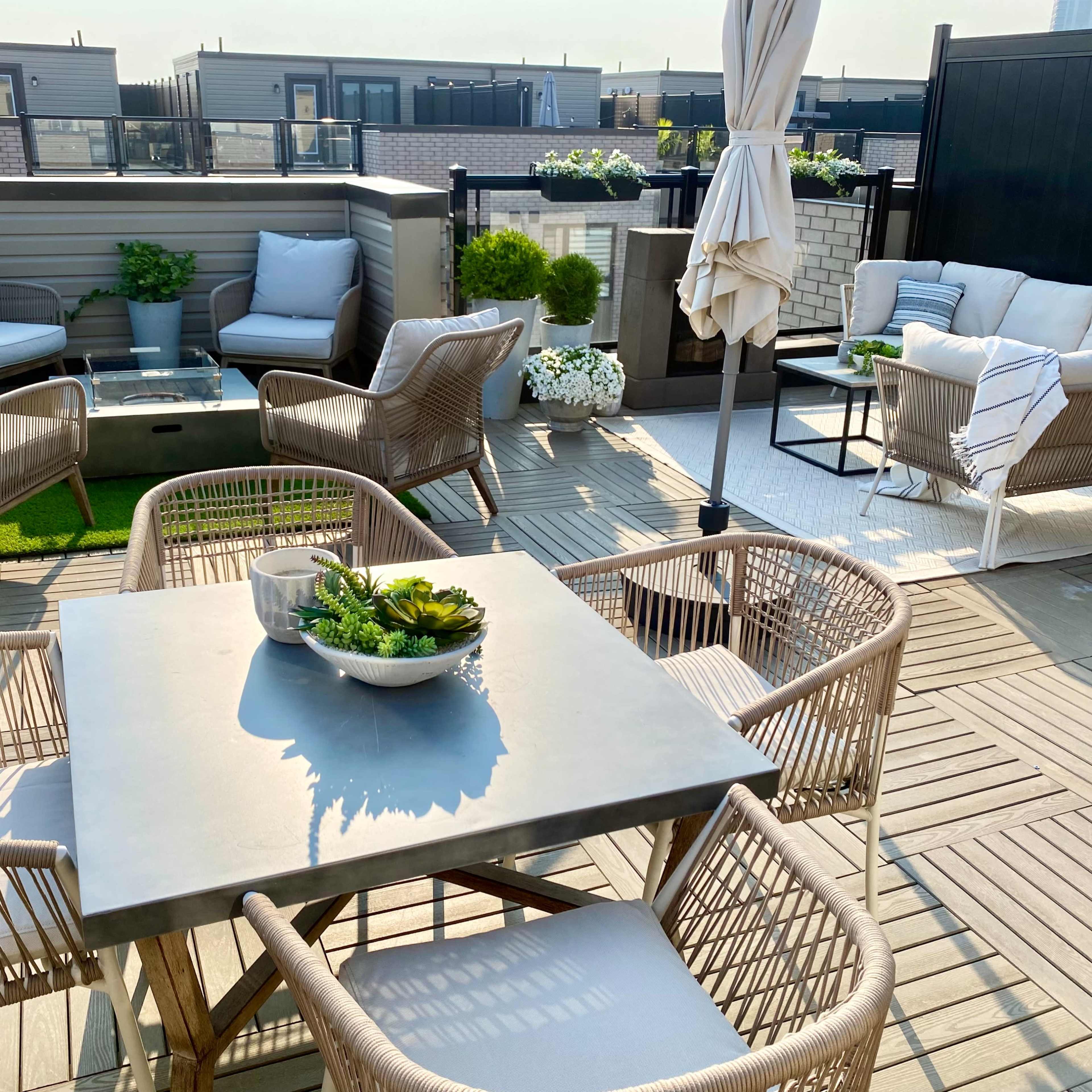 A rooftop terrace features a dining table surrounded by four chairs, with various seating areas and potted plants in the background.