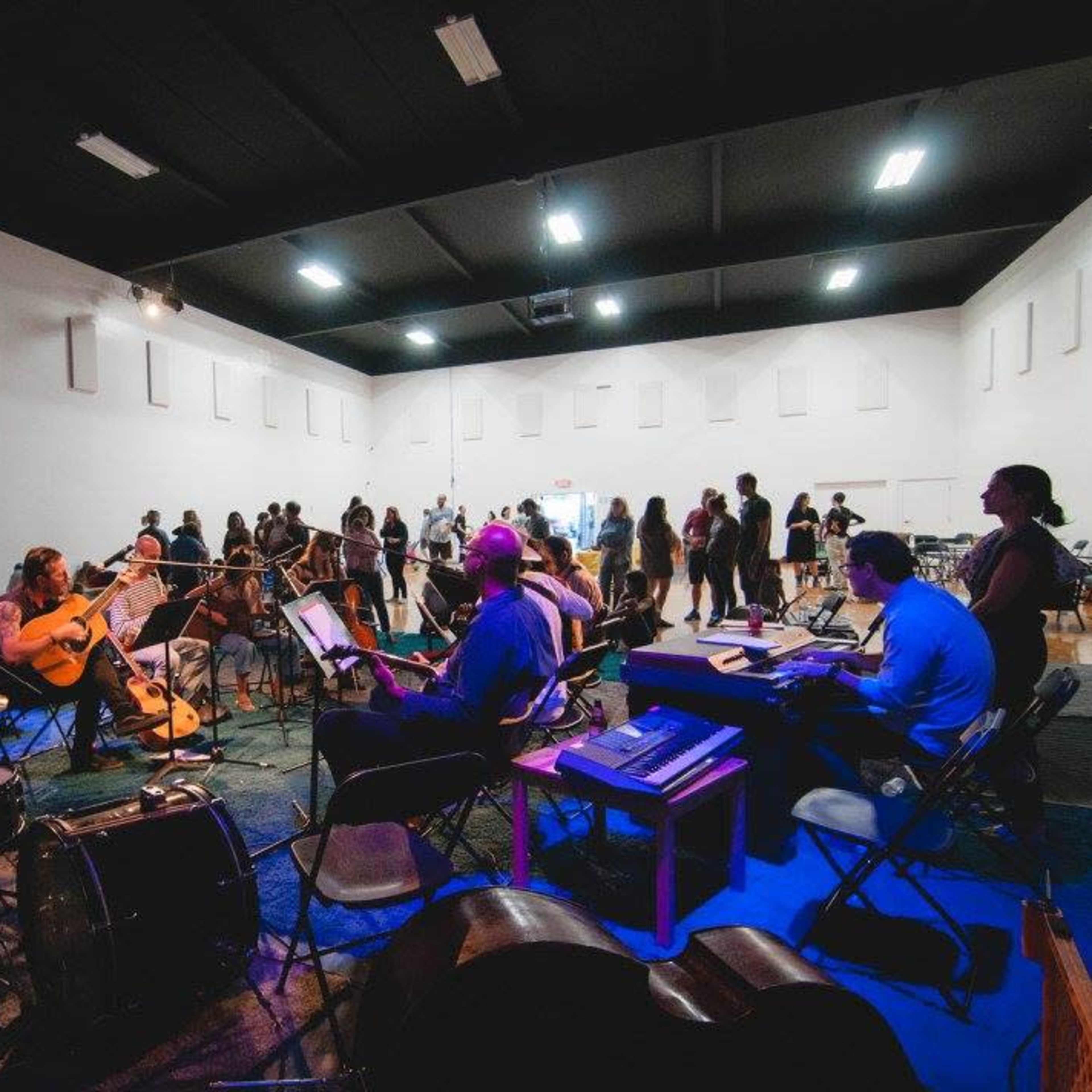 A group of musicians plays instruments in a large, open room while others mingle and move around.