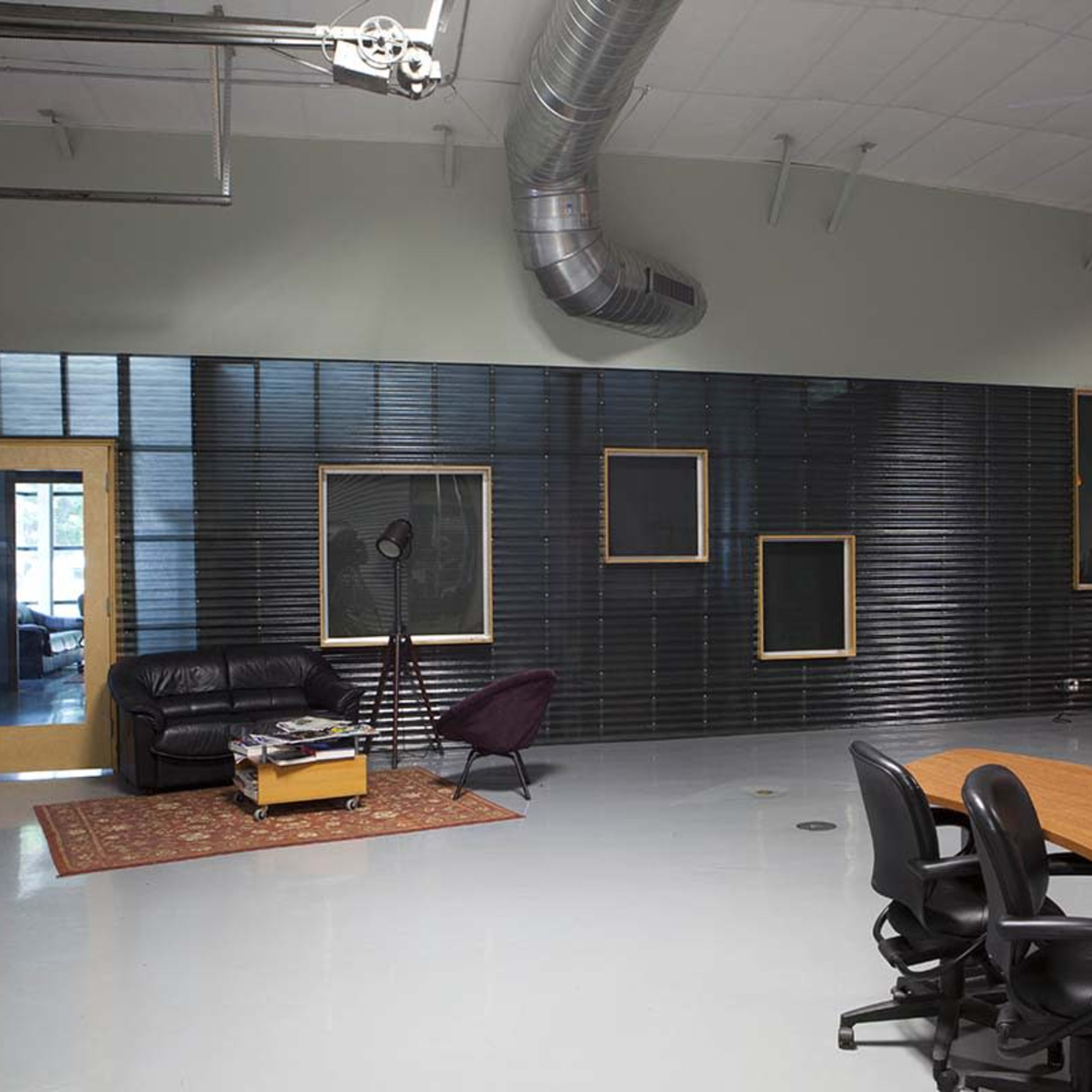 A modern, open office space with a seating area featuring a couch and chairs, a large meeting table, and a kitchen area in the background.