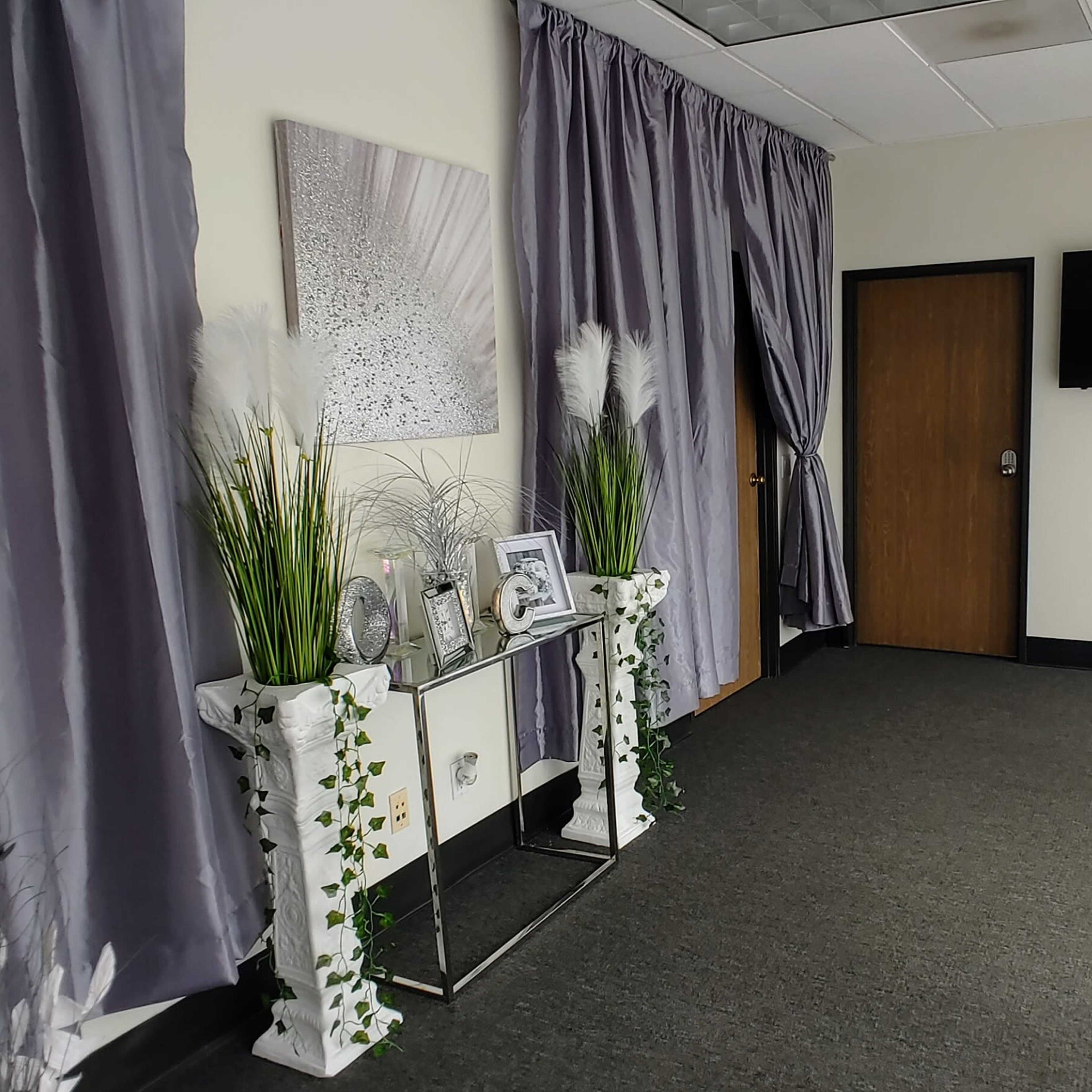 The room features gray curtains, a console table with decorative items, and a television mounted on the wall next to a door.