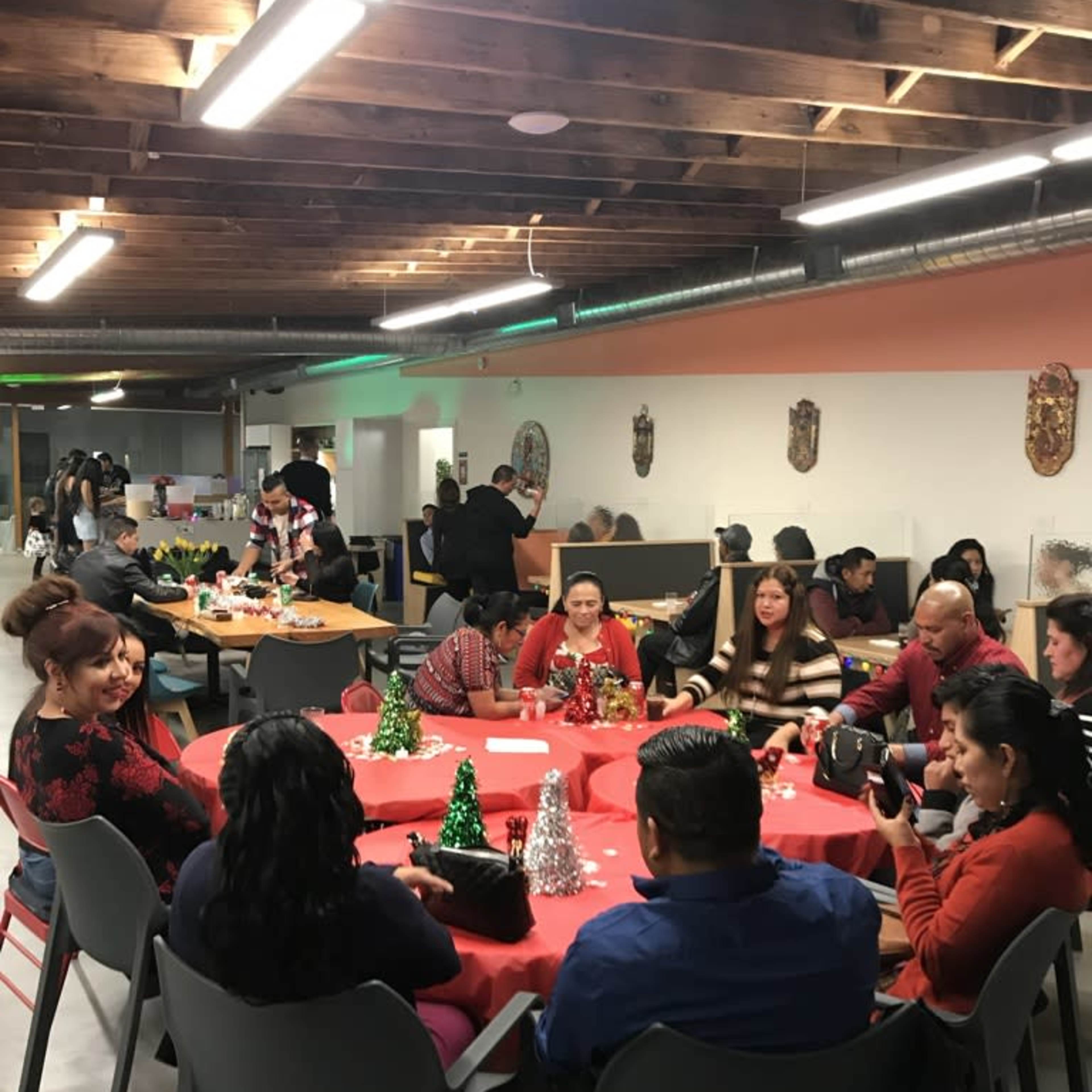 A group of people sits around decorated tables in a community gathering space, with some engaging in conversations and others arranging festive decorations.