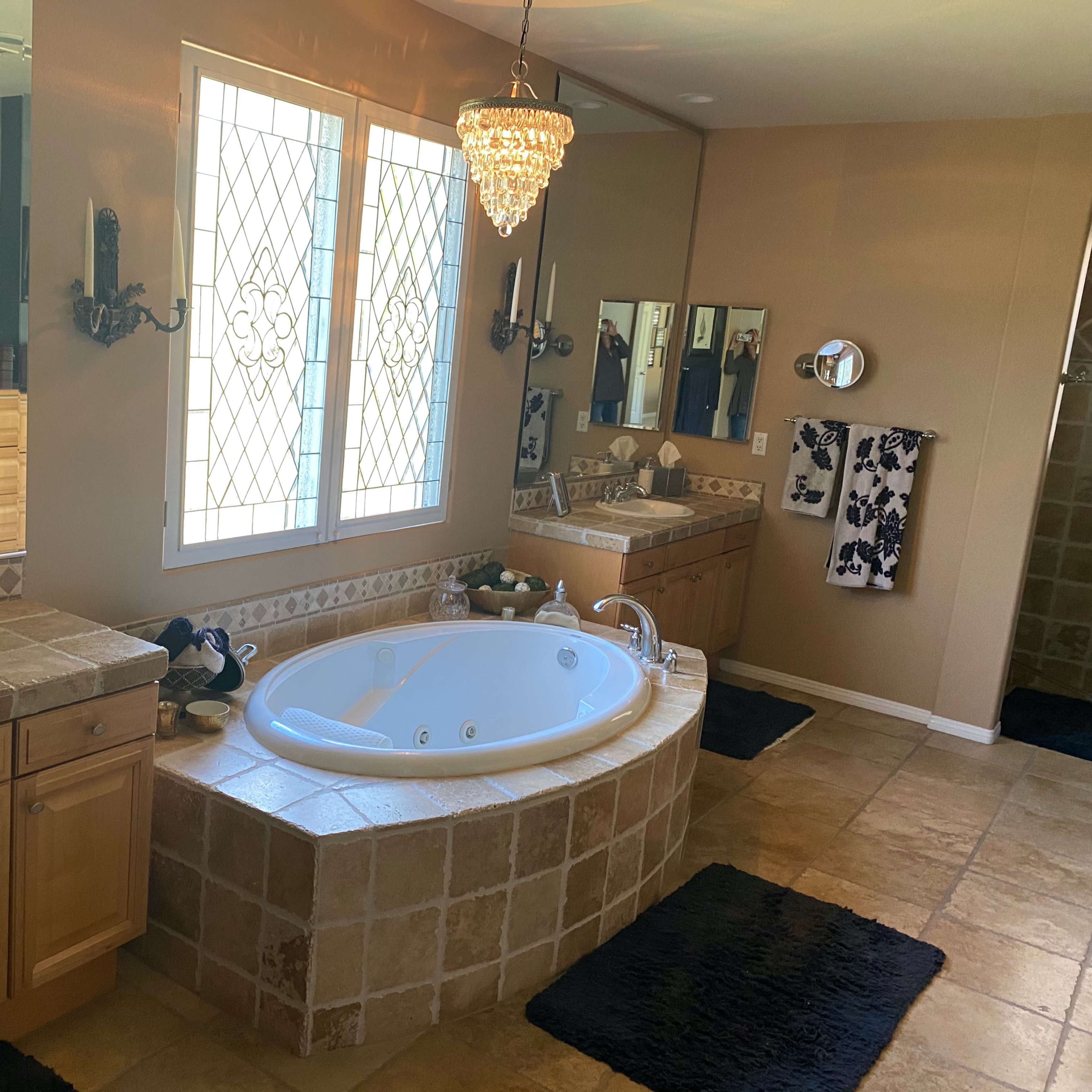 A spacious bathroom featuring a large bathtub, double sinks, a chandelier, and tiled flooring.