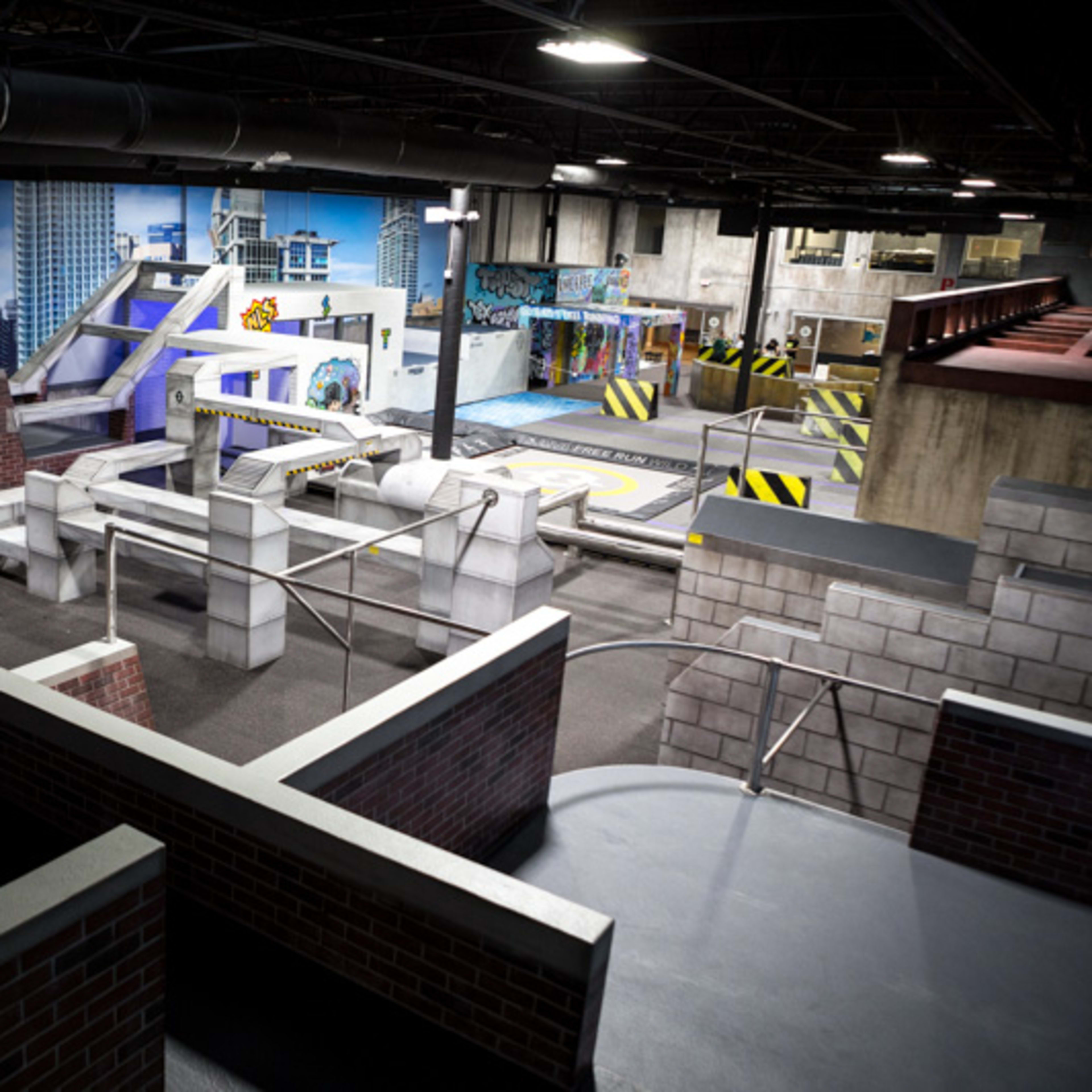 An indoor parkour training facility with various obstacles, ramps, and a graffiti-covered wall in a city-themed setting.
