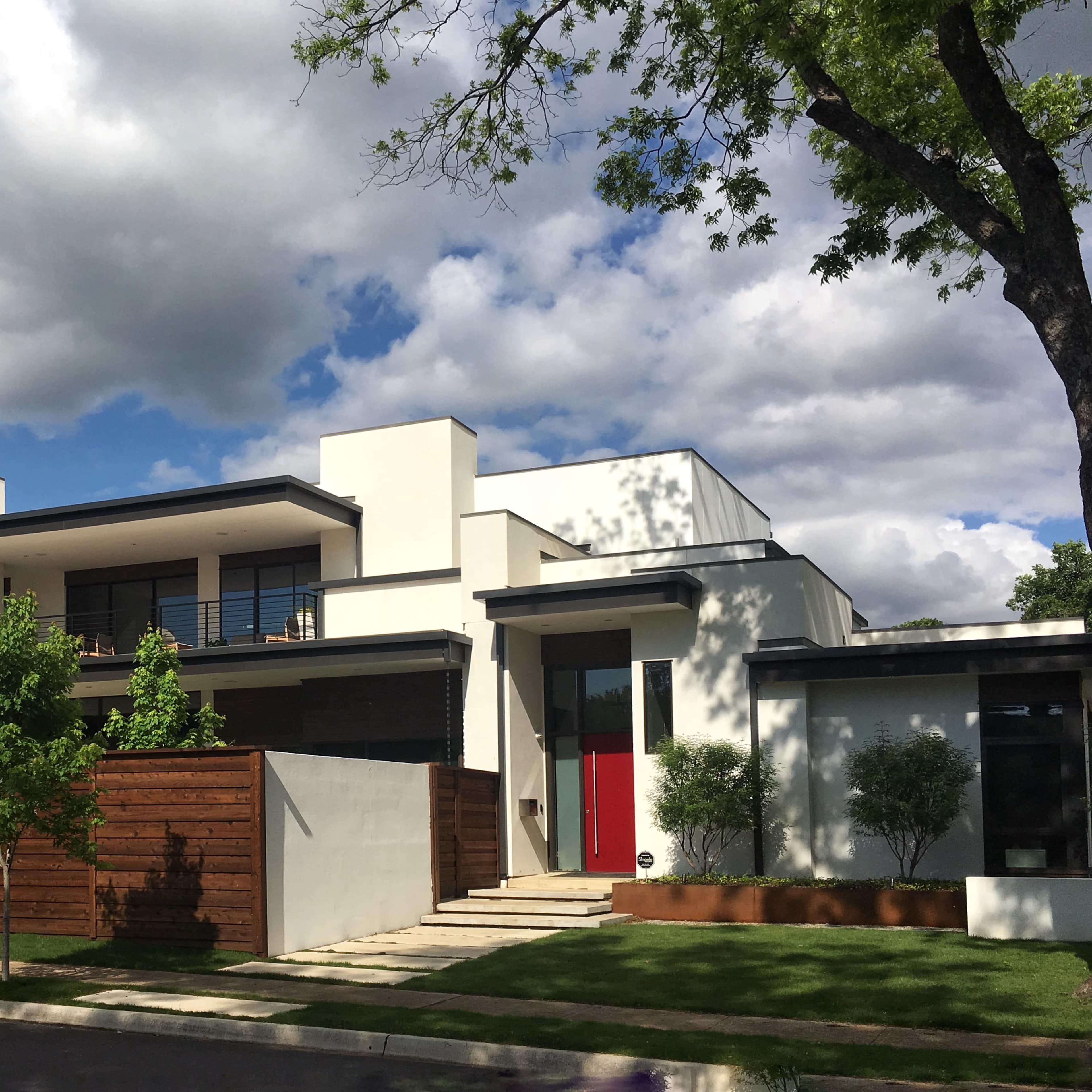 A modern two-story house features a red front door, large windows, and a wooden fence surrounding the yard.