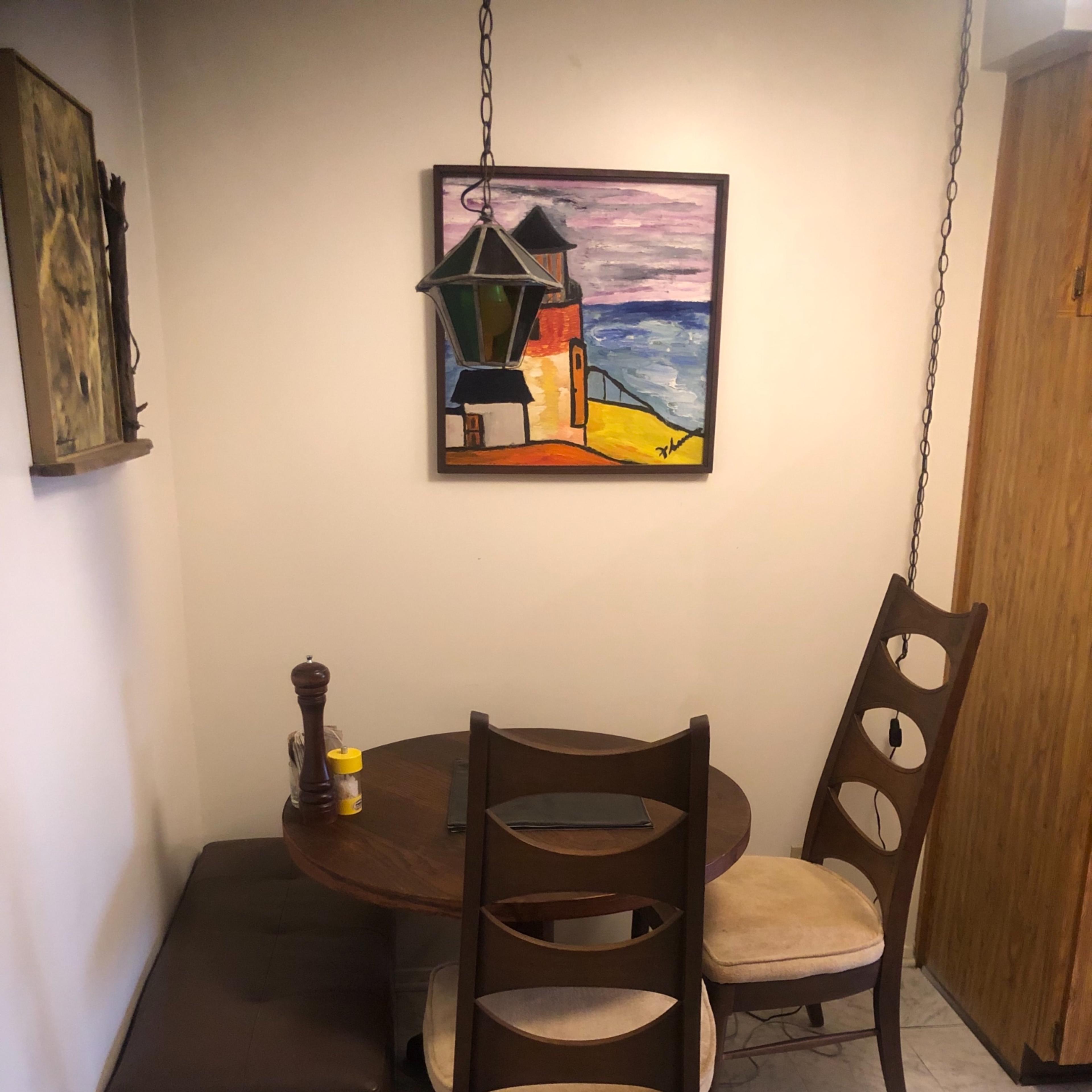 A small dining area features a round wooden table with two chairs and a painting hanging on the wall.