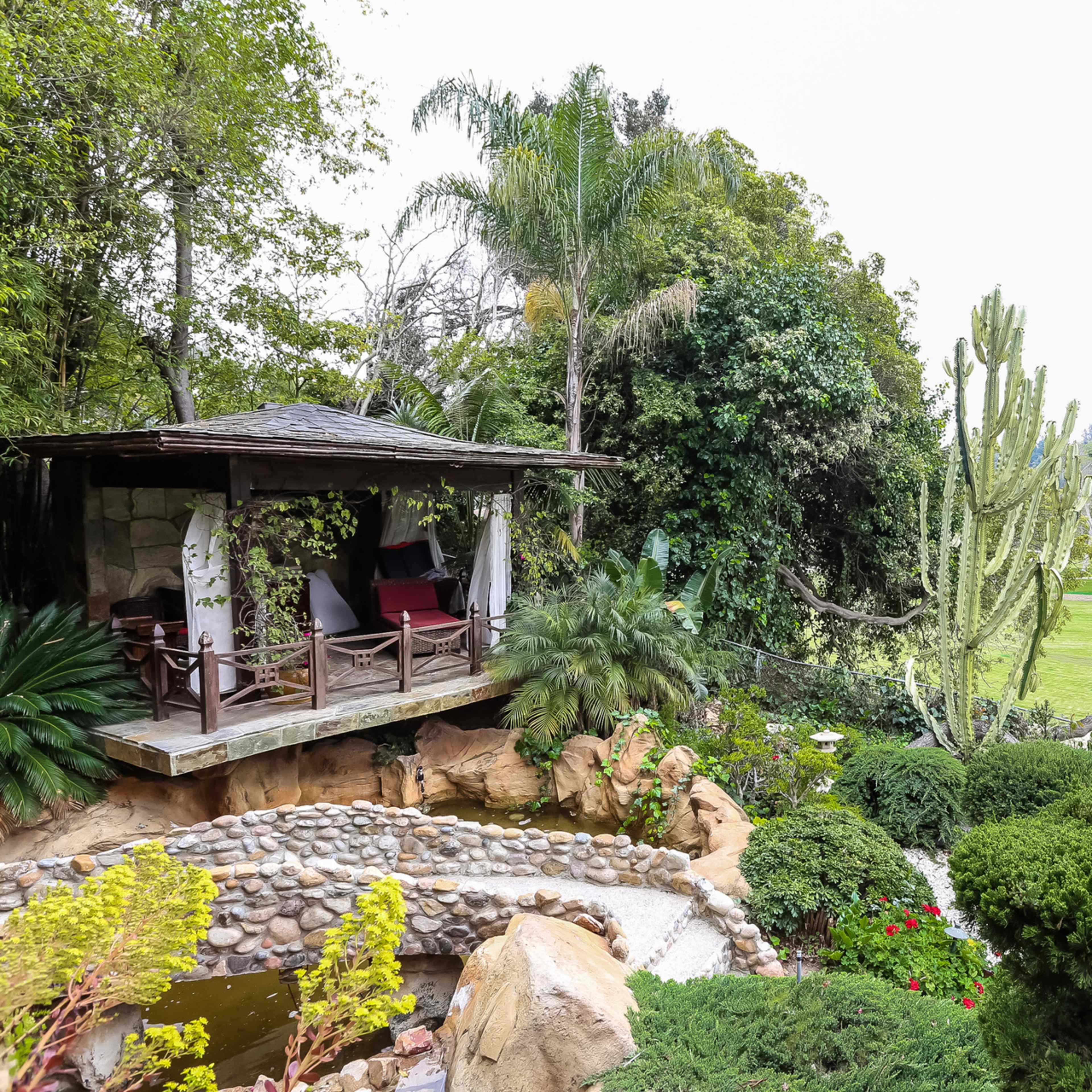 A landscaped garden features a gazebo surrounded by lush greenery, cacti, and a small pond.