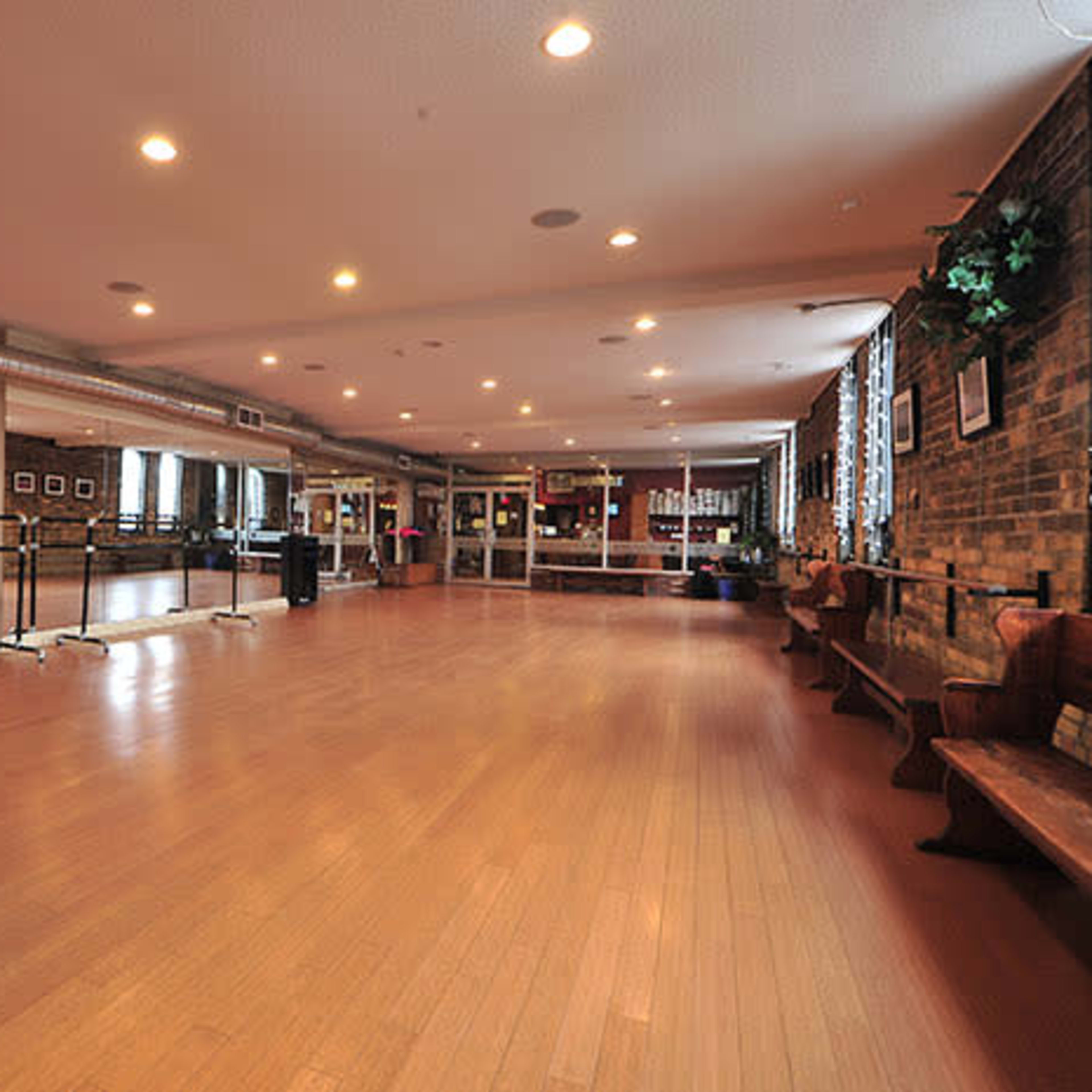 A spacious dance studio with wooden floors, mirrored walls, and benches along one side.