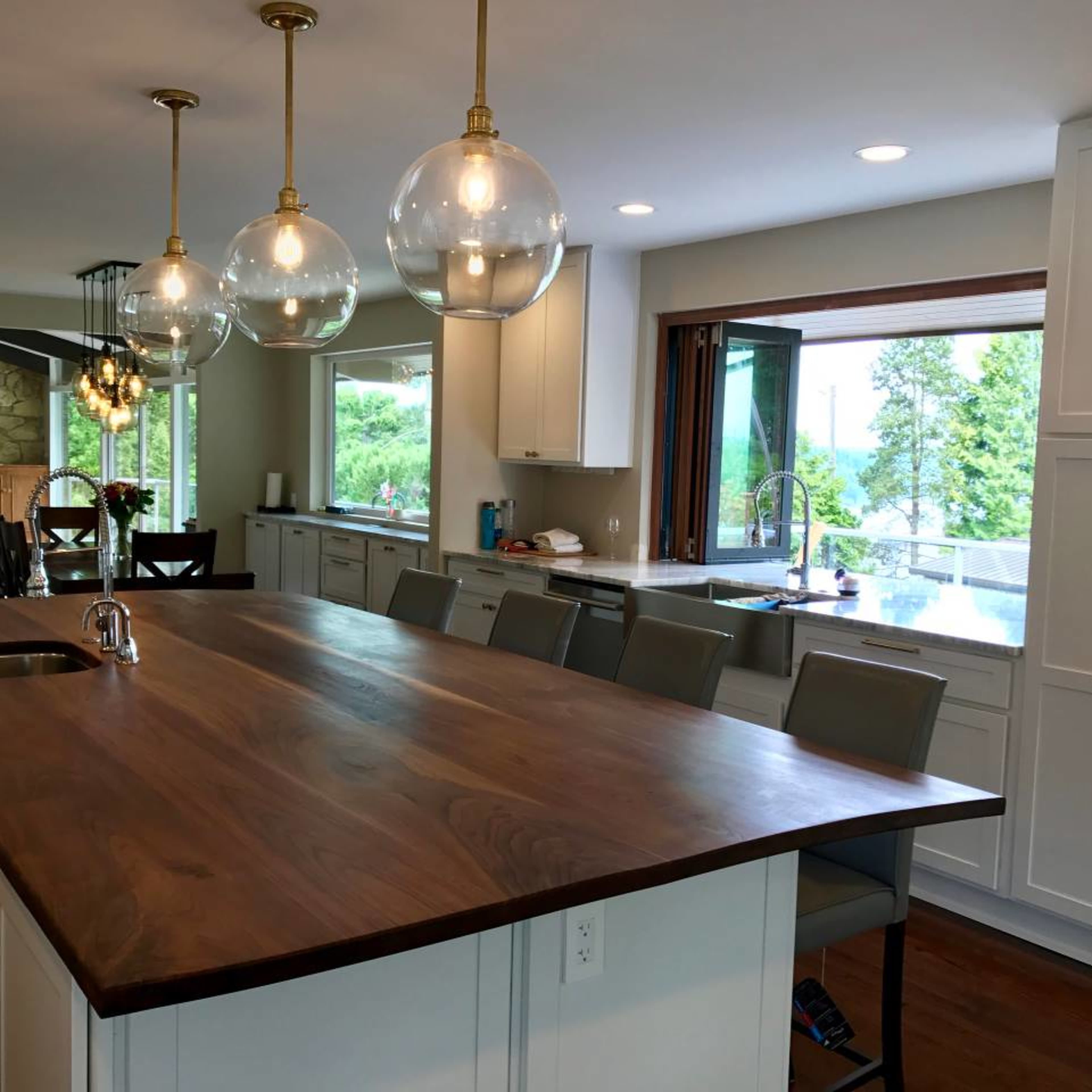 A modern kitchen with a large wooden island, pendant lights overhead, and a view of trees through a window.