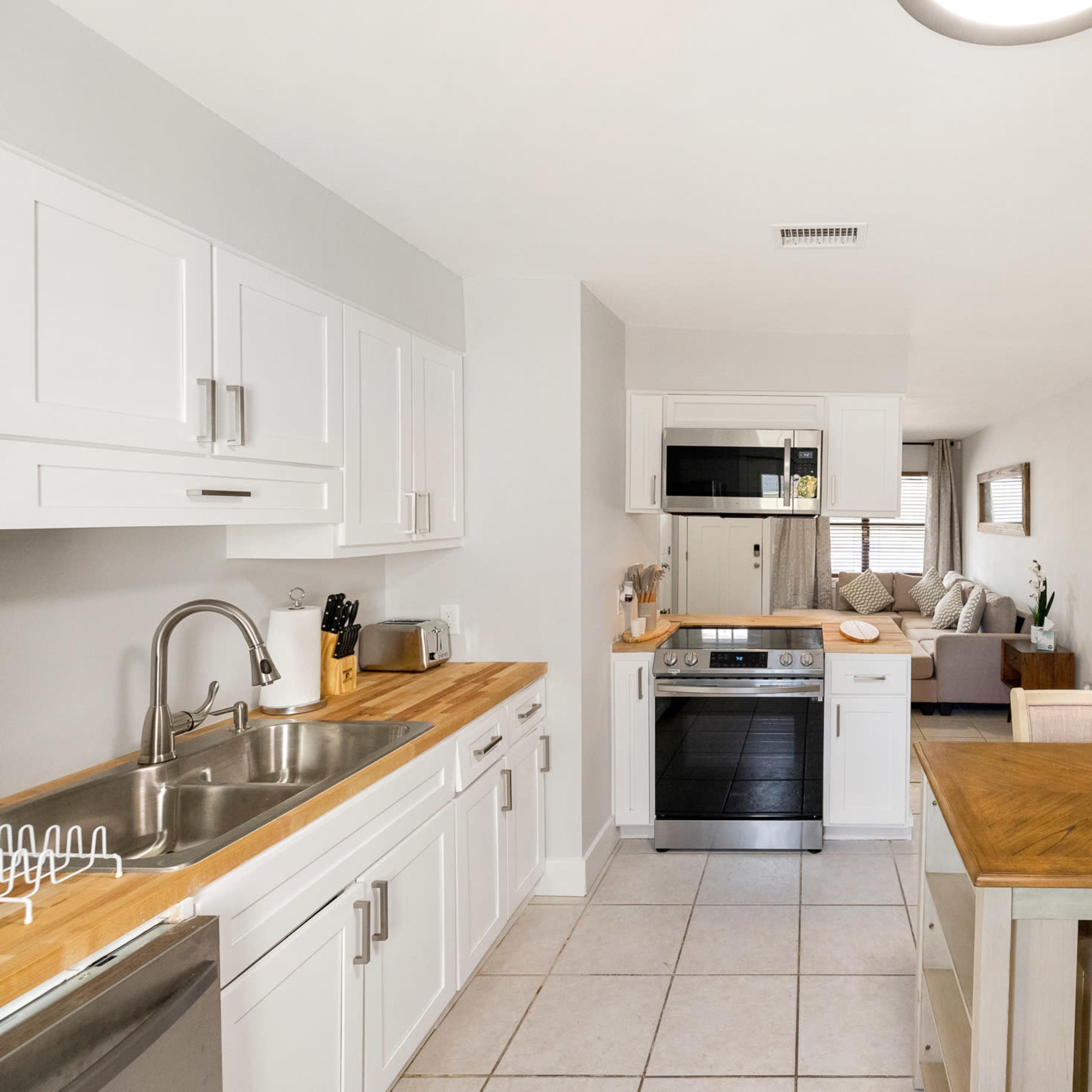 A modern kitchen features white cabinetry, stainless steel appliances, and a wooden dining table with chairs.