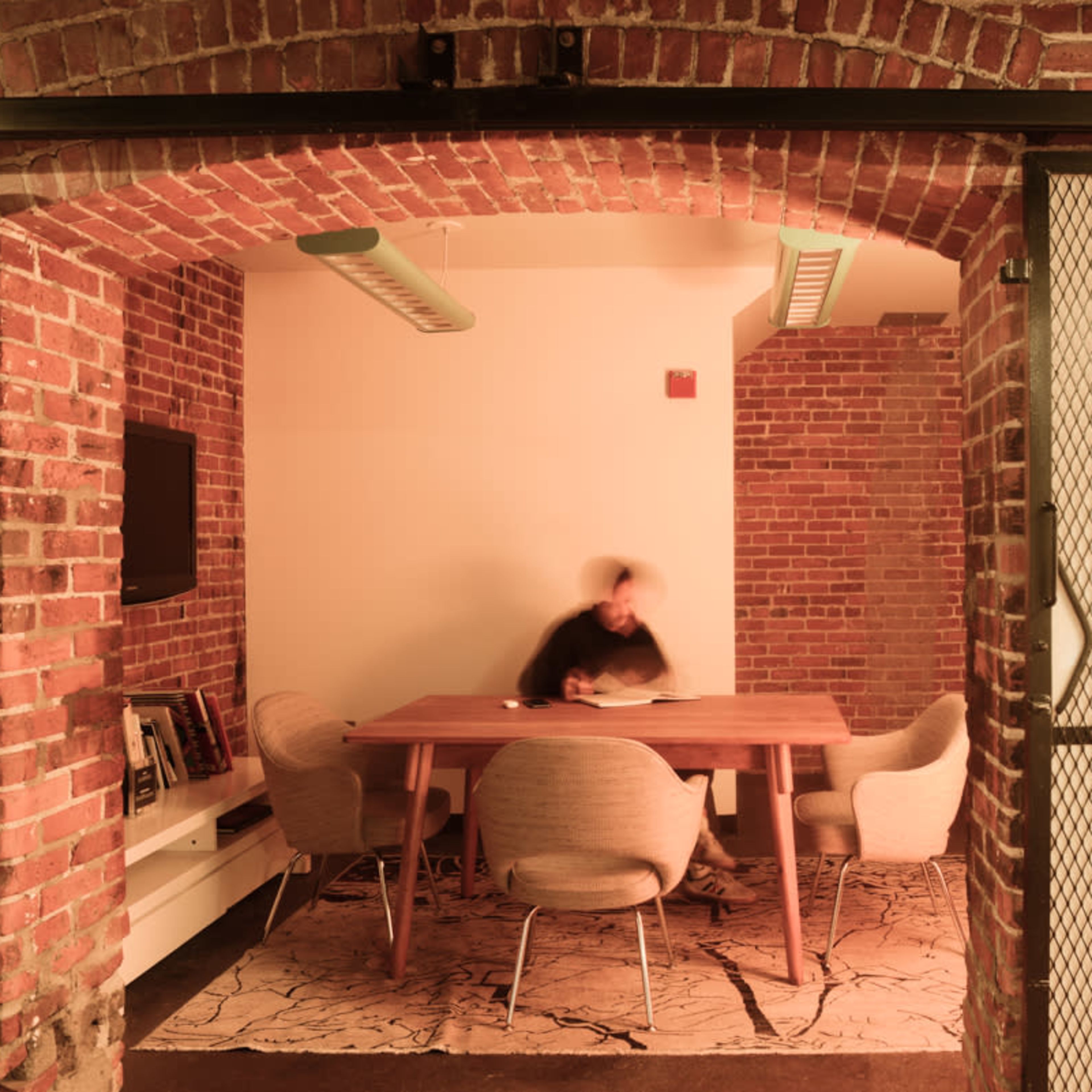 A meeting room with a large table and four chairs, characterized by exposed brick walls and ambient lighting.