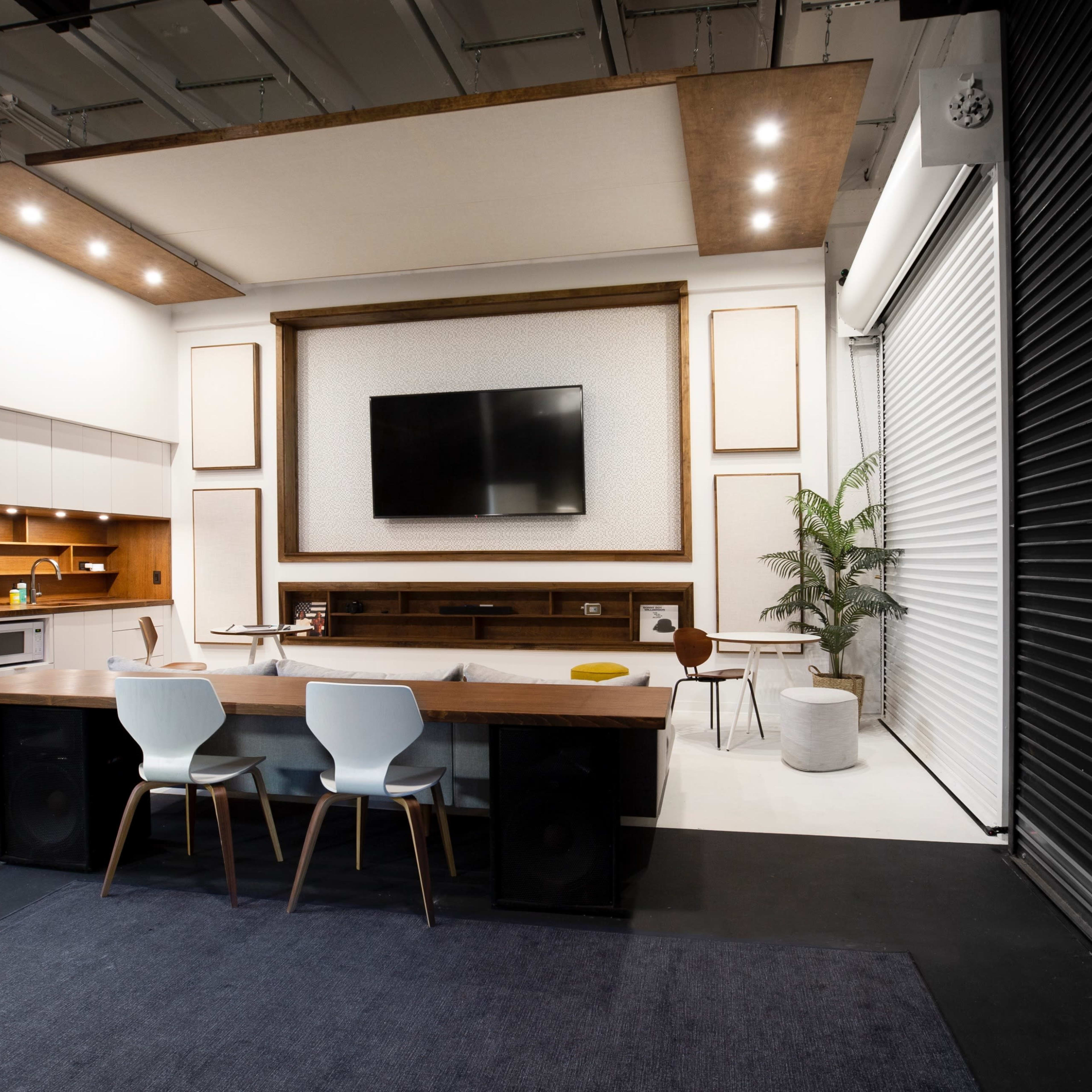 A modern indoor space featuring a kitchen area, a large television mounted on a wall, a dining table with chairs, and a potted plant.