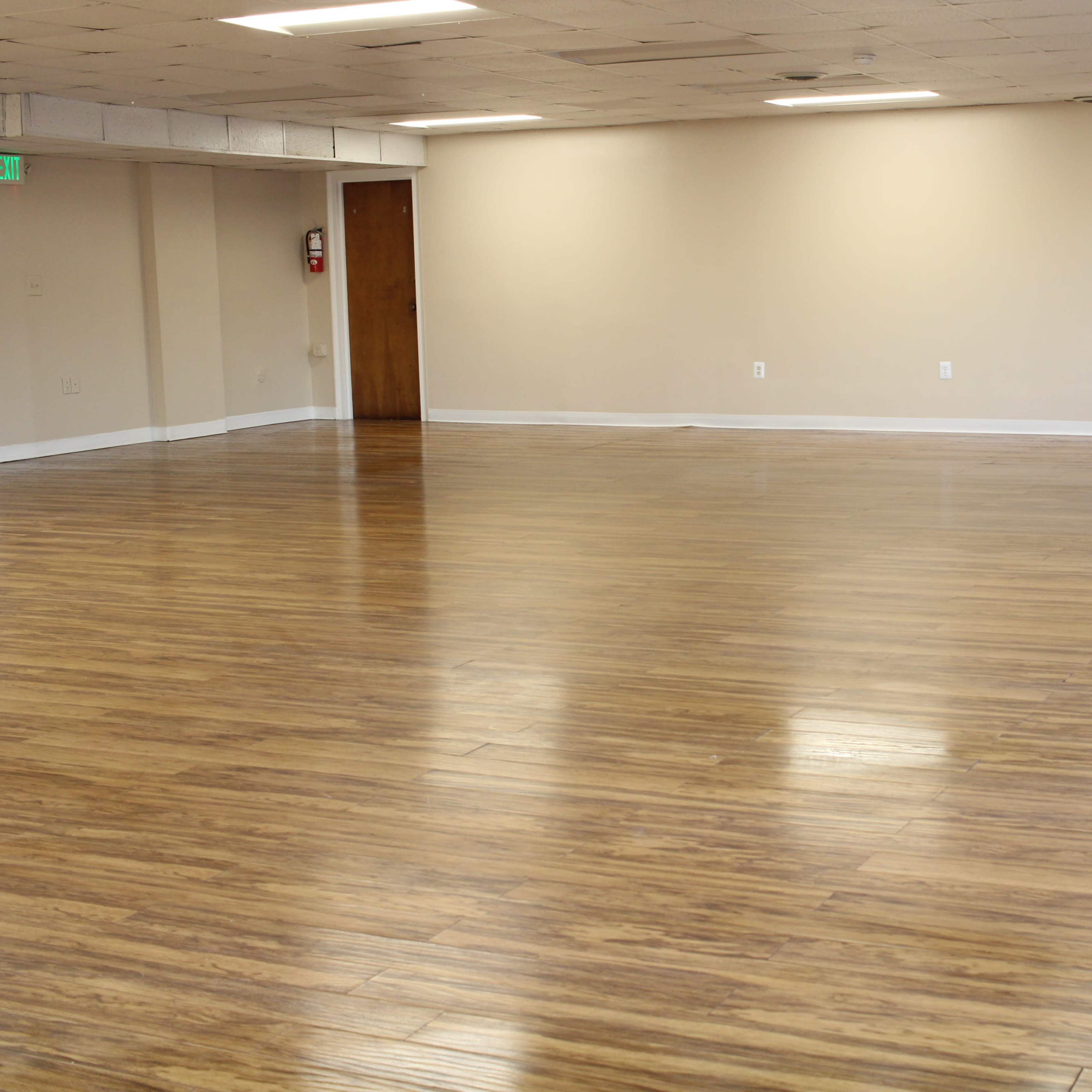 A empty room with wooden flooring and cream-colored walls, featuring a single door at one end.