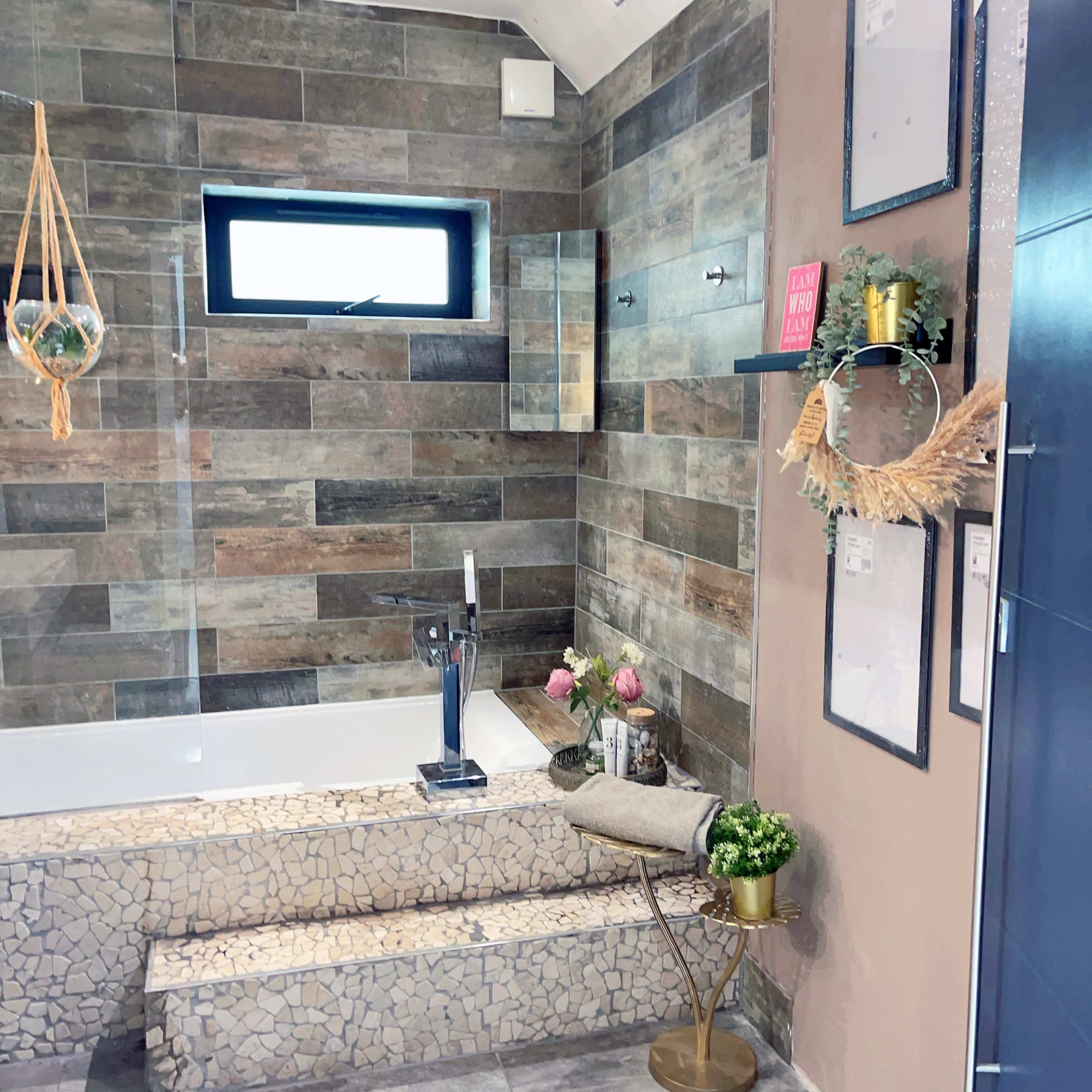 A modern bathroom featuring a bathtub on a mosaic-tiled platform, with a variety of decorative elements including plants and framed artwork on the walls.