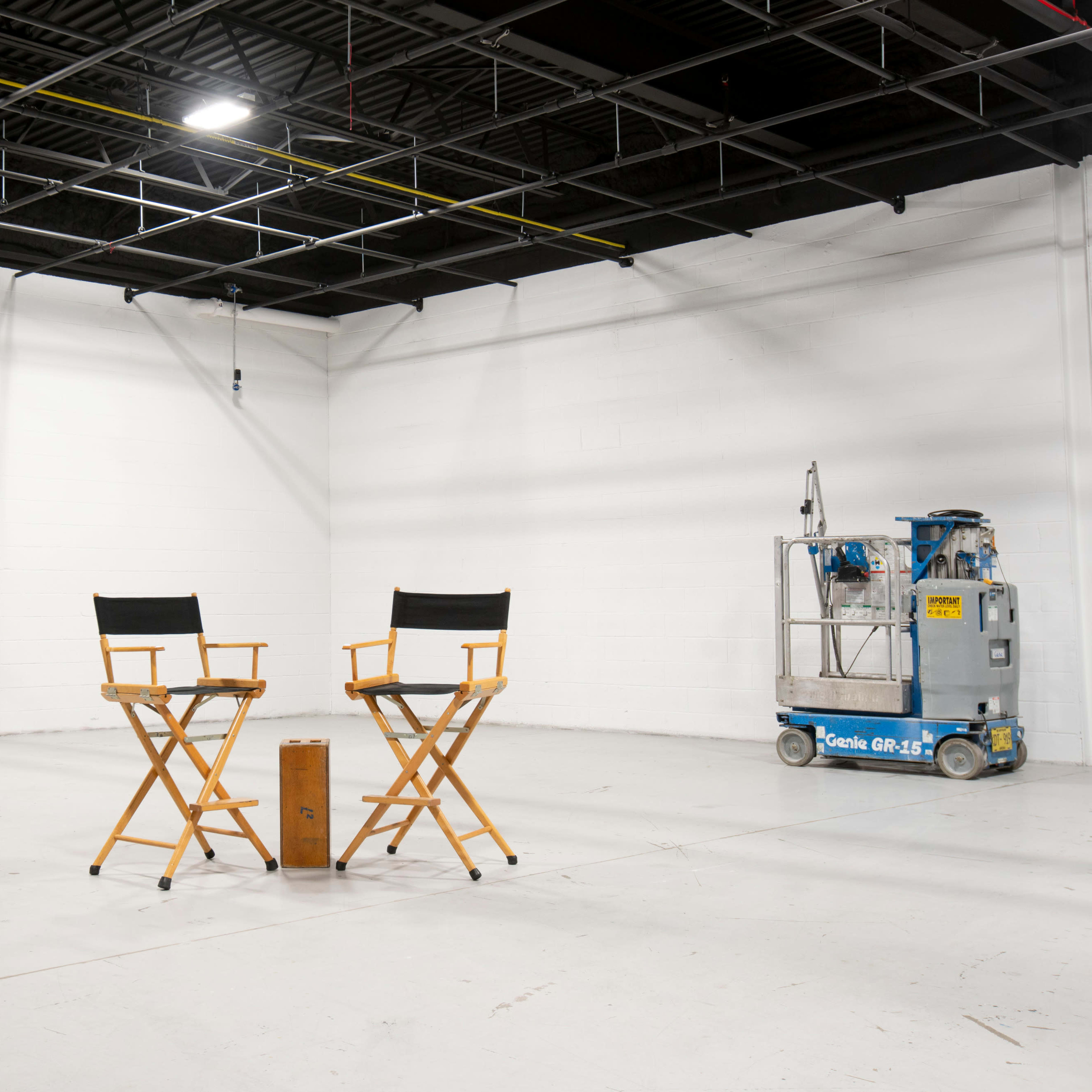 Two director's chairs placed on a bare concrete floor, accompanied by a small table and a ladder against the wall.
