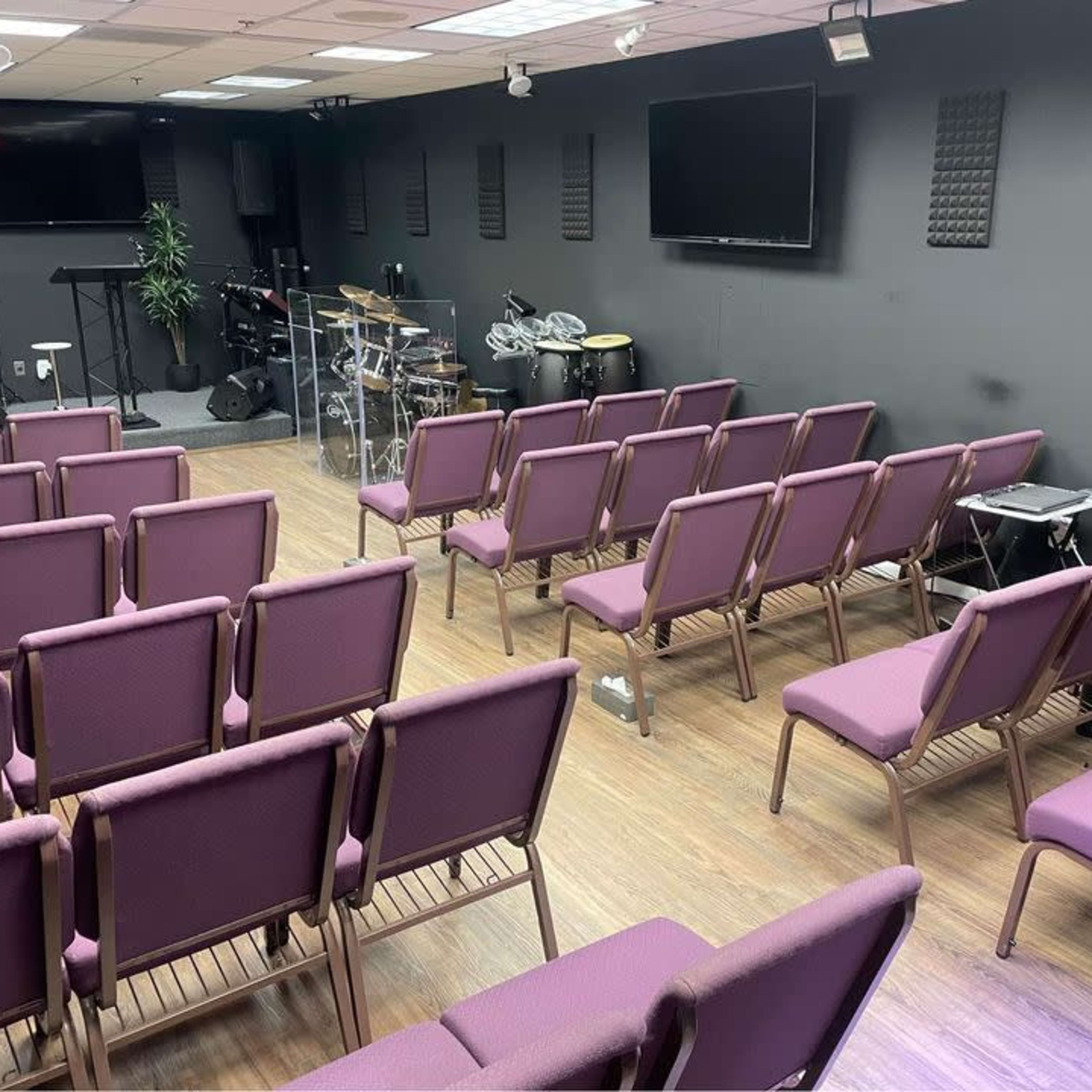 A musical performance space with purple chairs arranged in rows facing a small stage and instruments in the background.