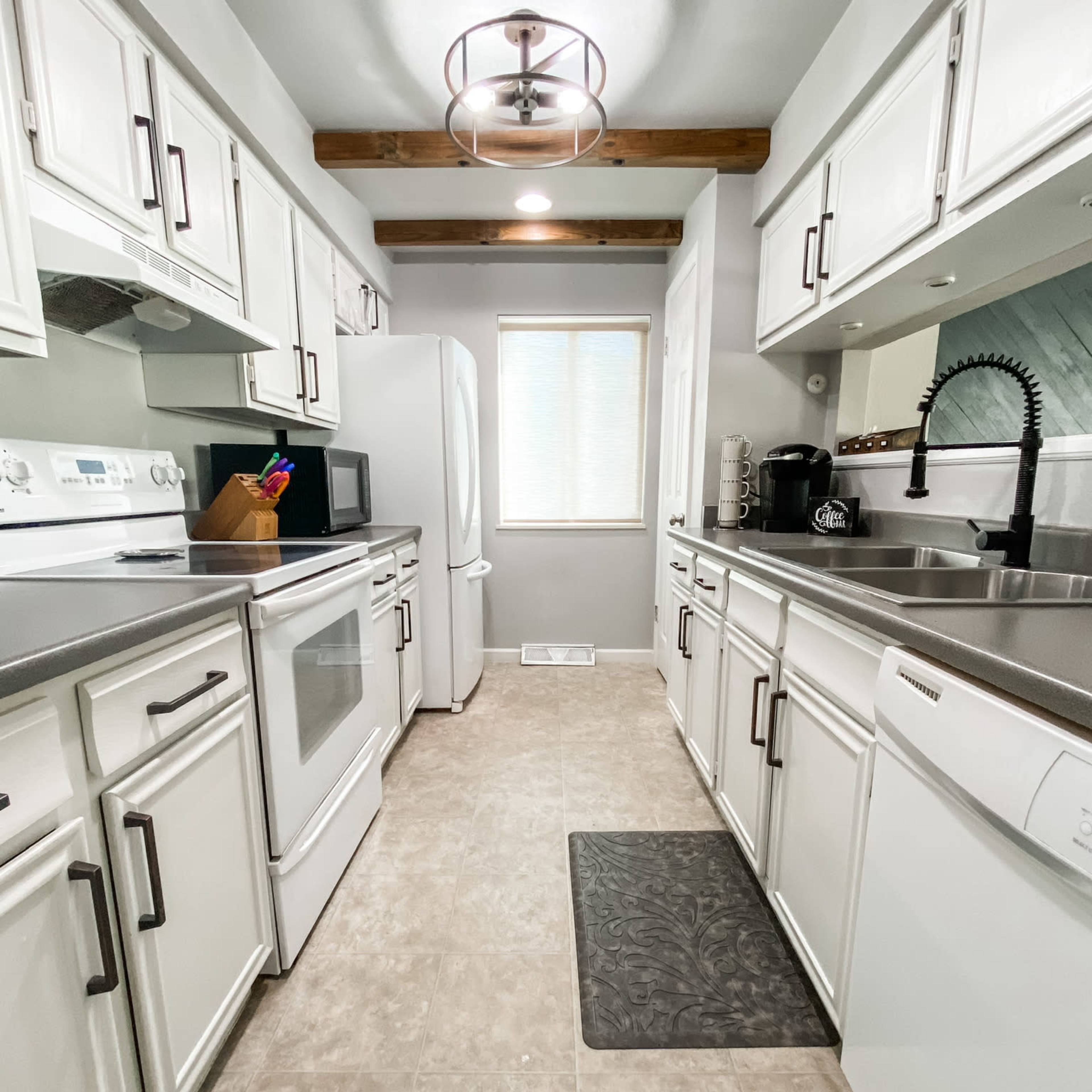 A modern kitchen with white cabinetry, stainless steel appliances, and a window allowing natural light to enter.