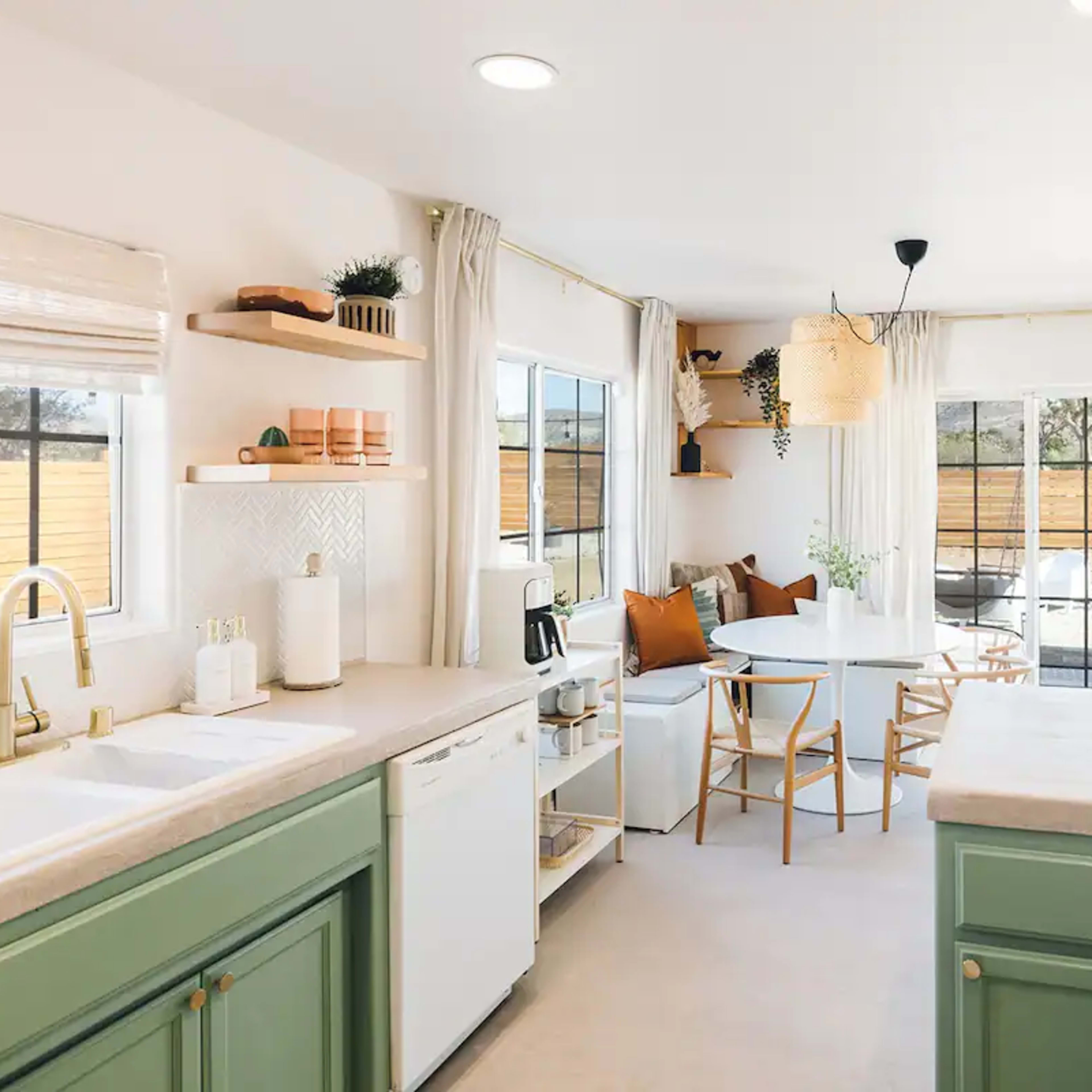 A modern kitchen features green cabinetry, a dining table with chairs, and ample natural light from large windows.
