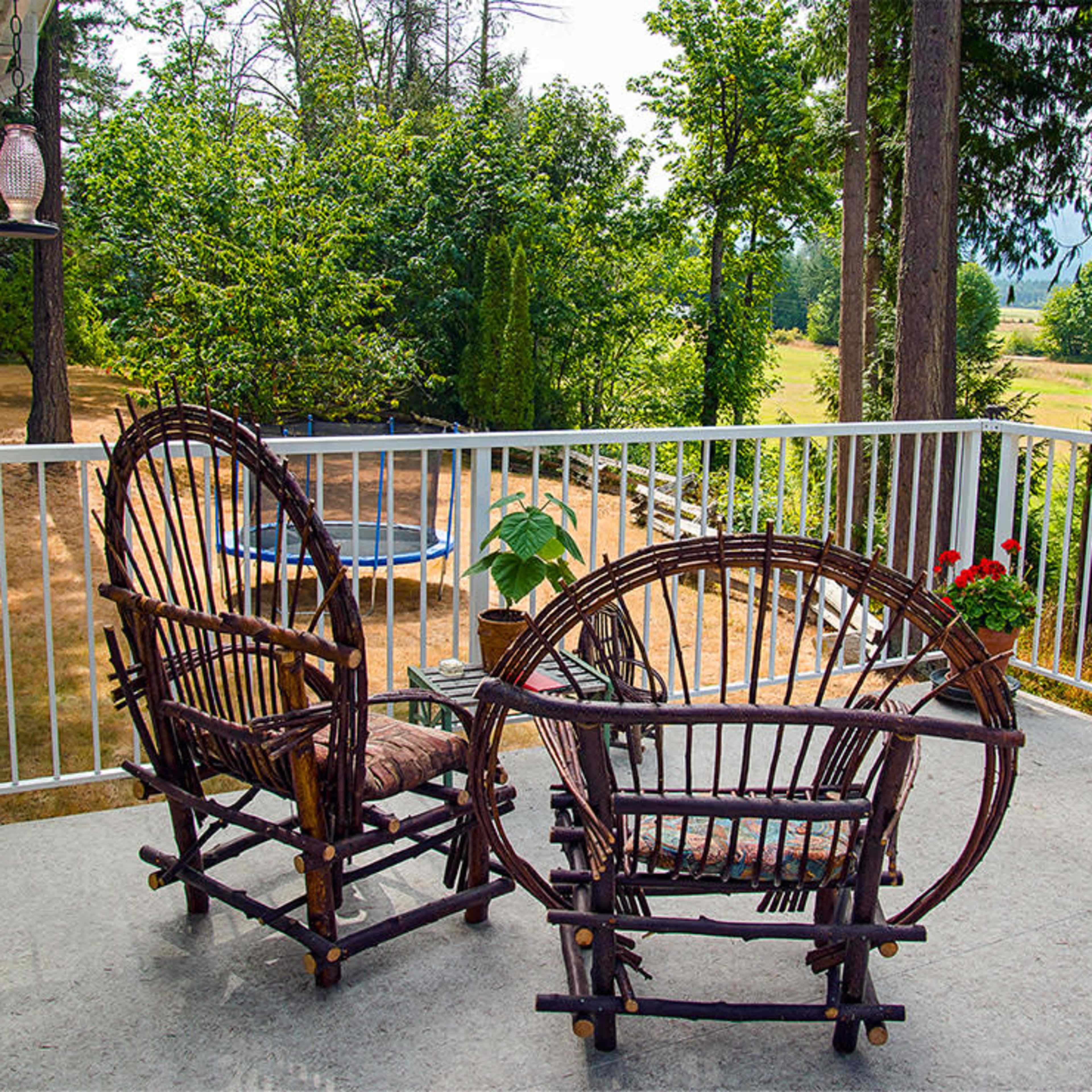 A pair of wicker chairs sits on a patio overlooking a grassy area and trees.
