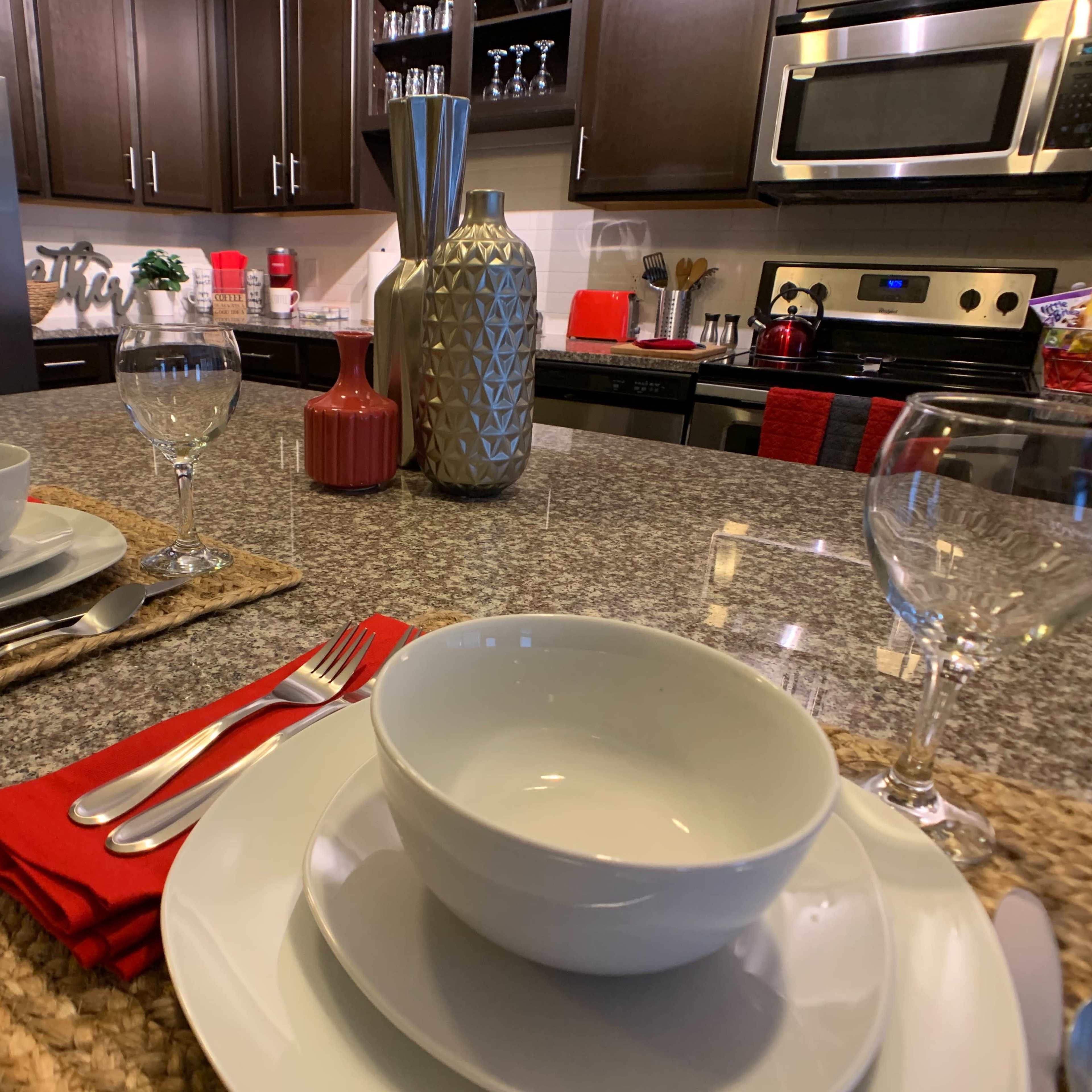 A modern kitchen countertop set for a meal, featuring polished dinnerware, glassware, and decorative elements.