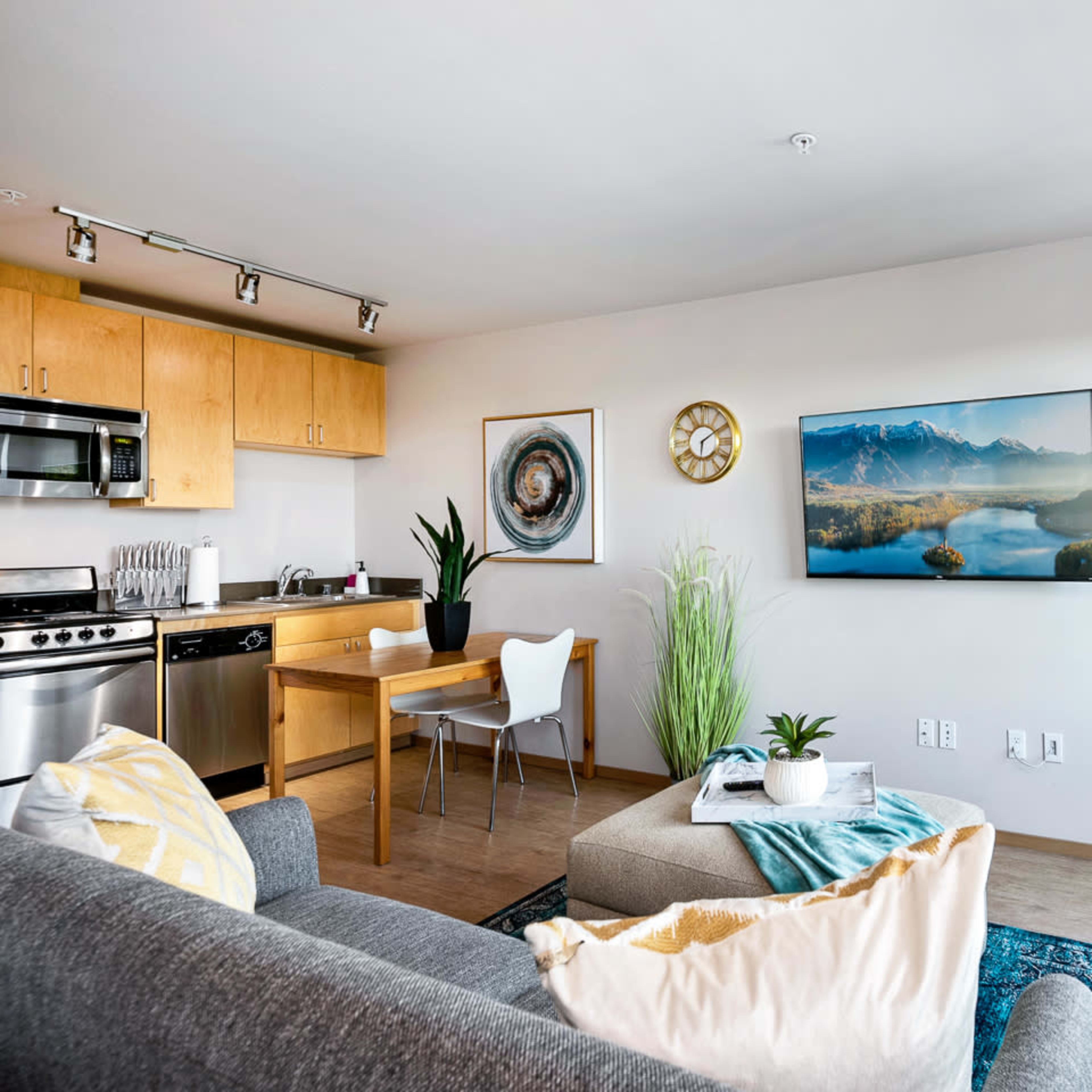 A modern living space with a kitchen area, a chair and dining table, a couch, and a large window displaying a scenic view.