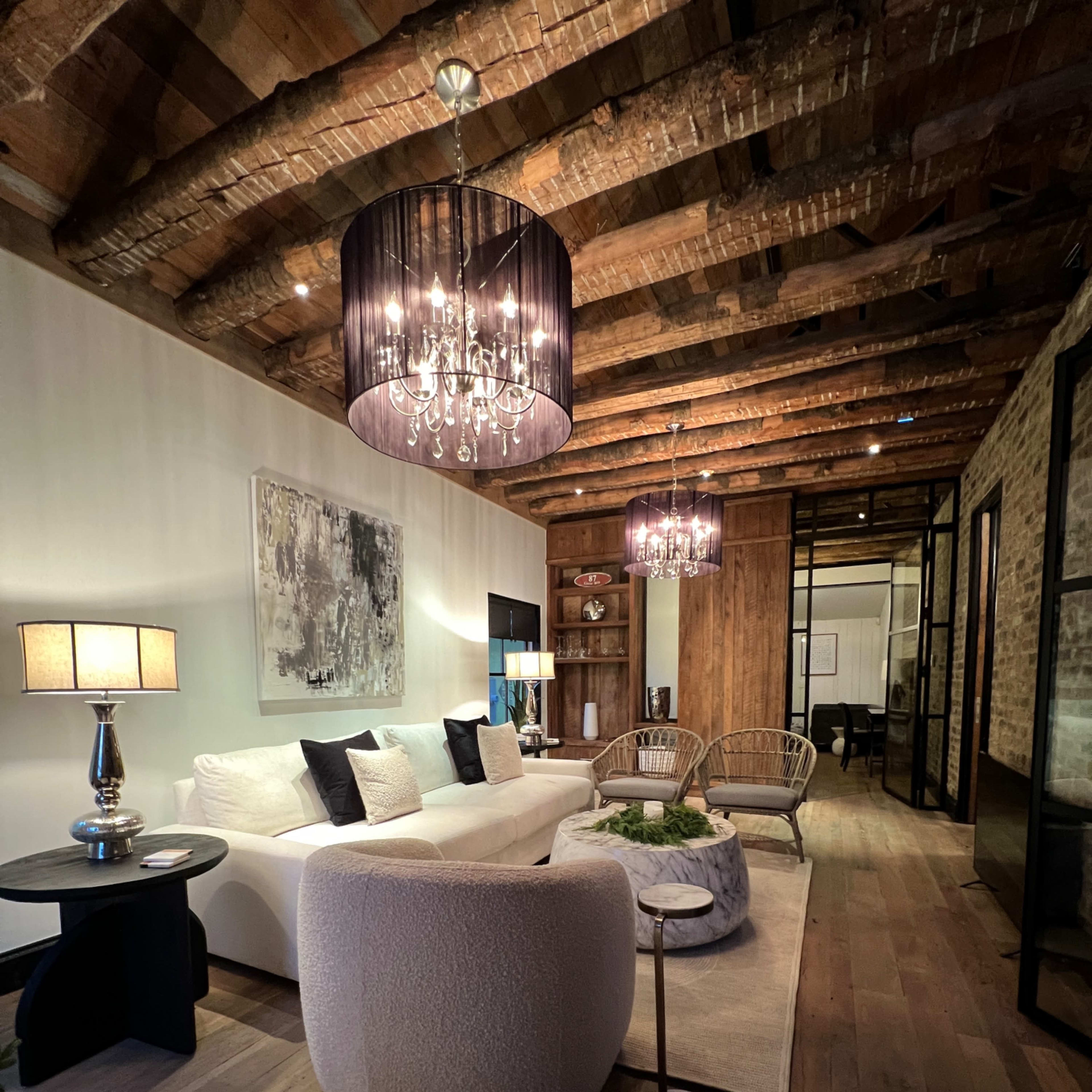 A modern living room with a white sofa, two rattan chairs, a coffee table, and exposed wooden beams on the ceiling.