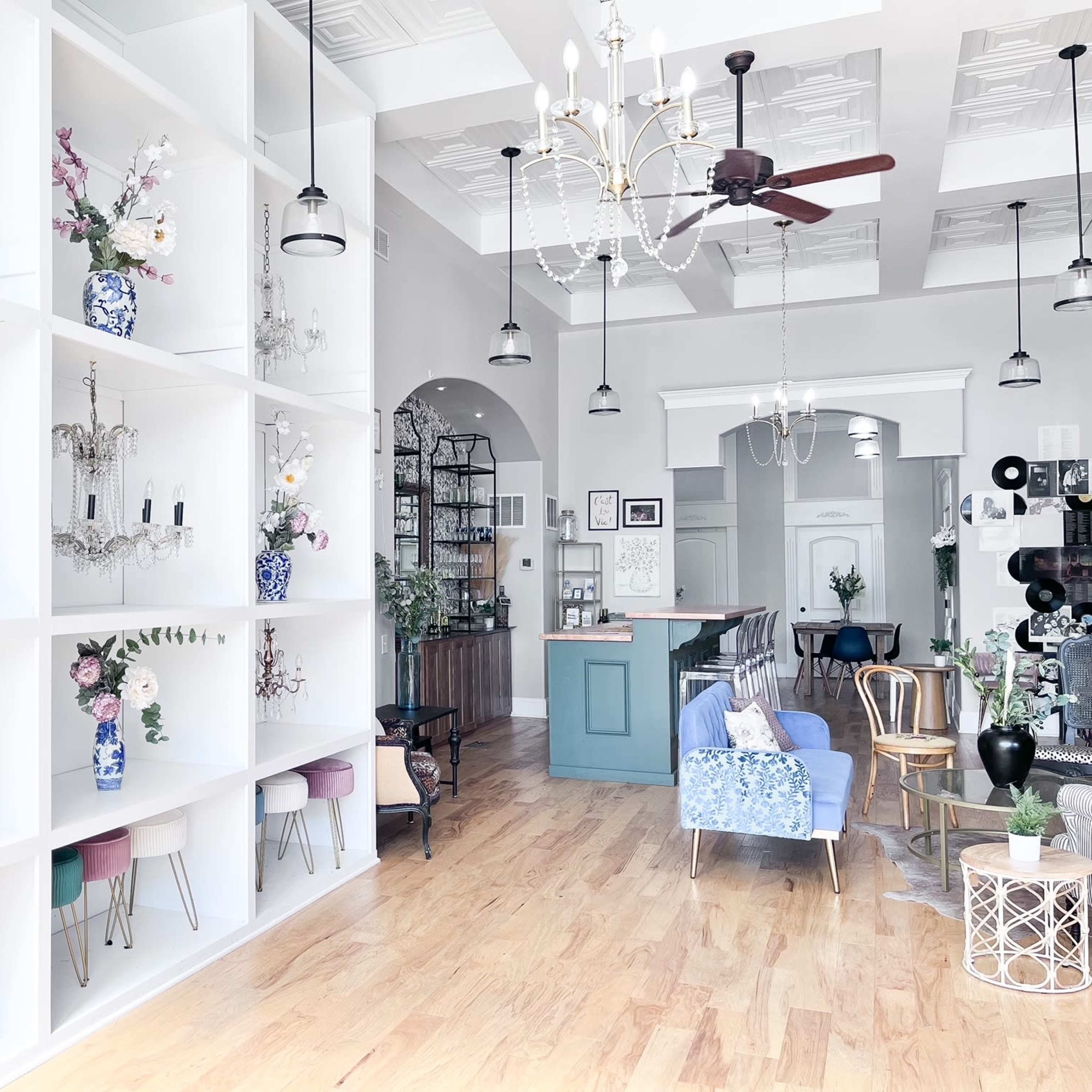A modern interior space with white shelves displaying decorative vases and chandeliers, complemented by a seating area and a bar counter.