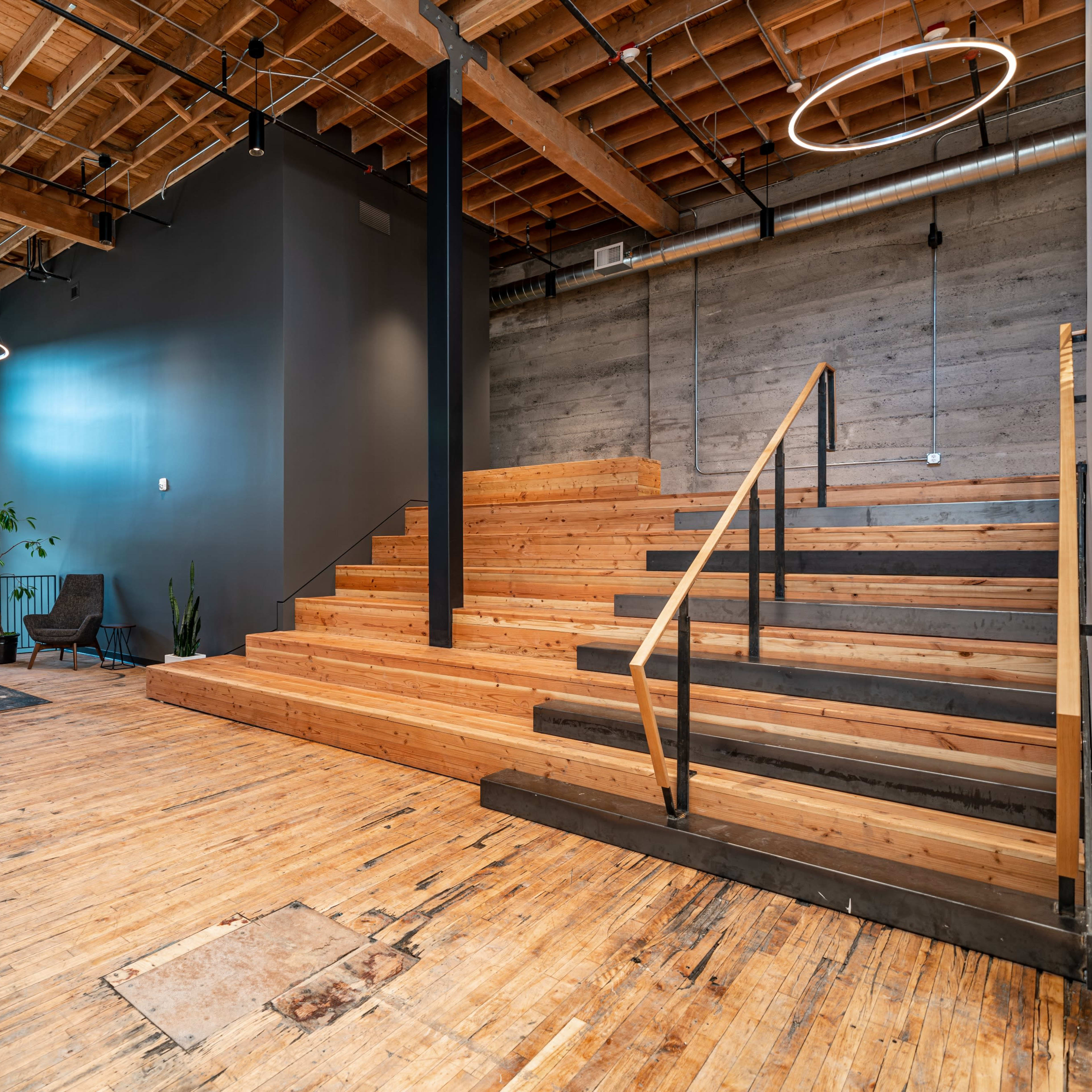 A modern interior with wooden stairs leading to a second level, large windows, and a clean, open space featuring minimal furniture and plants.