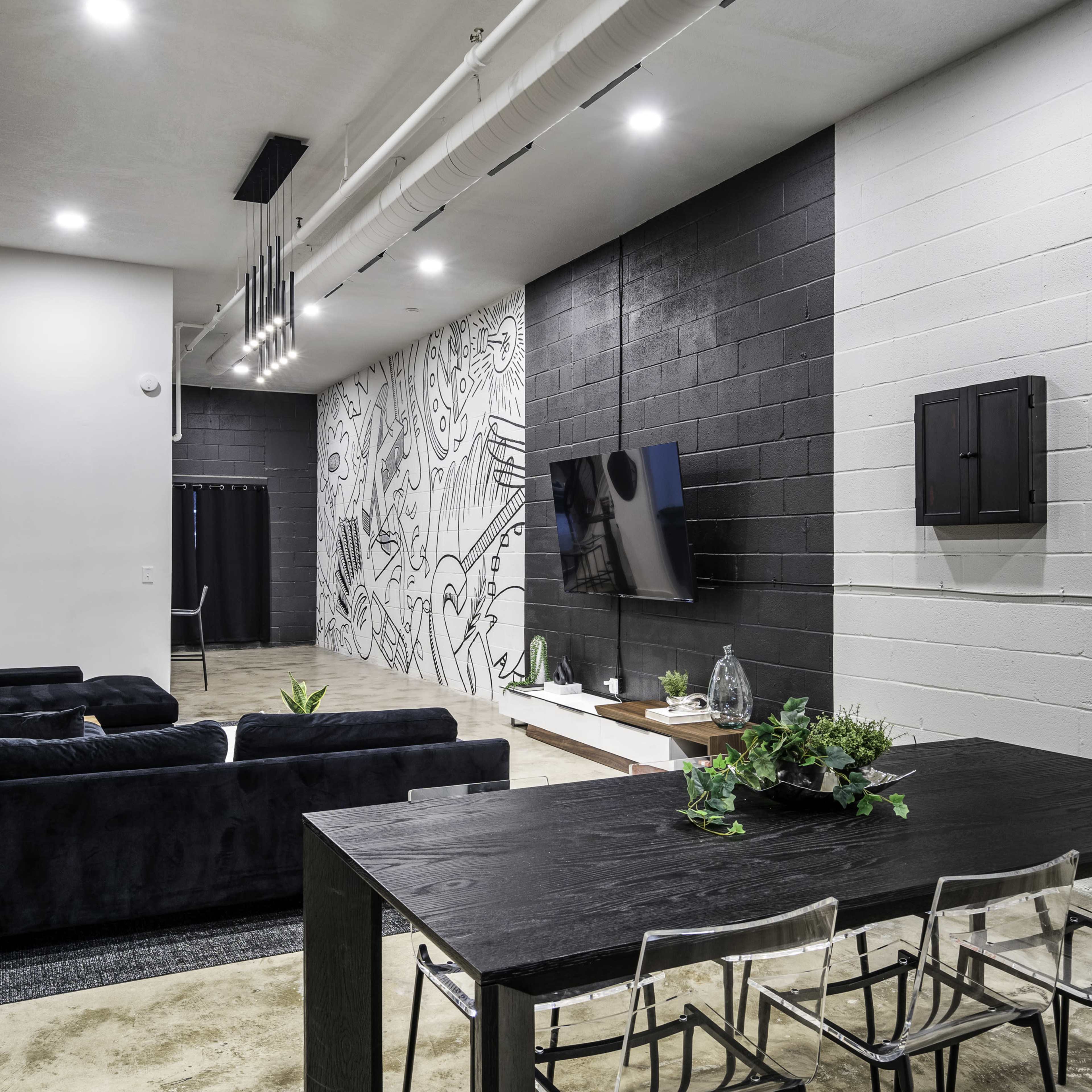 A modern interior space featuring a dining table with clear chairs, a black sofa, and a wall adorned with a mural.