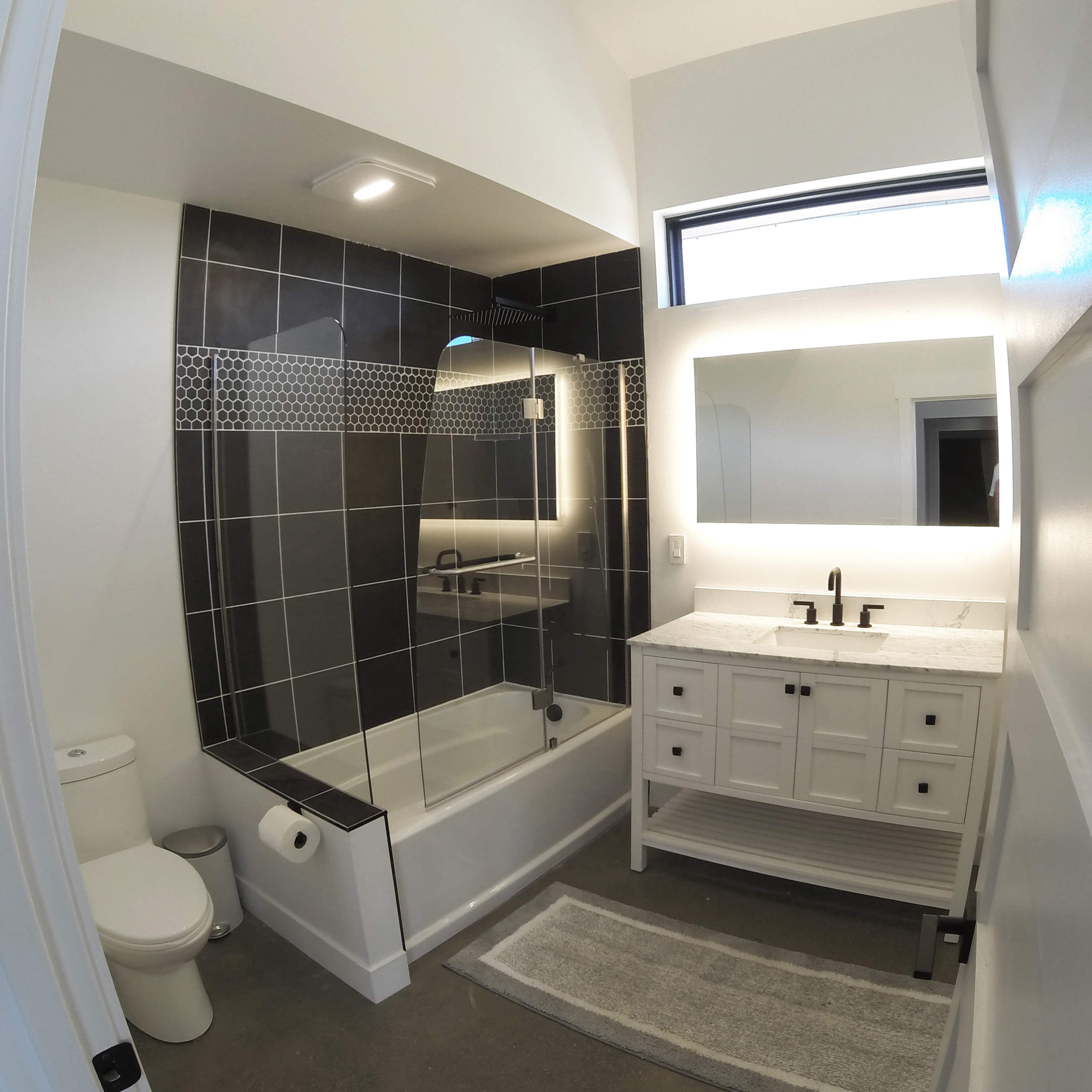A modern bathroom featuring a bathtub with a glass shower enclosure, a vanity with a white countertop, and black and white tiled walls.