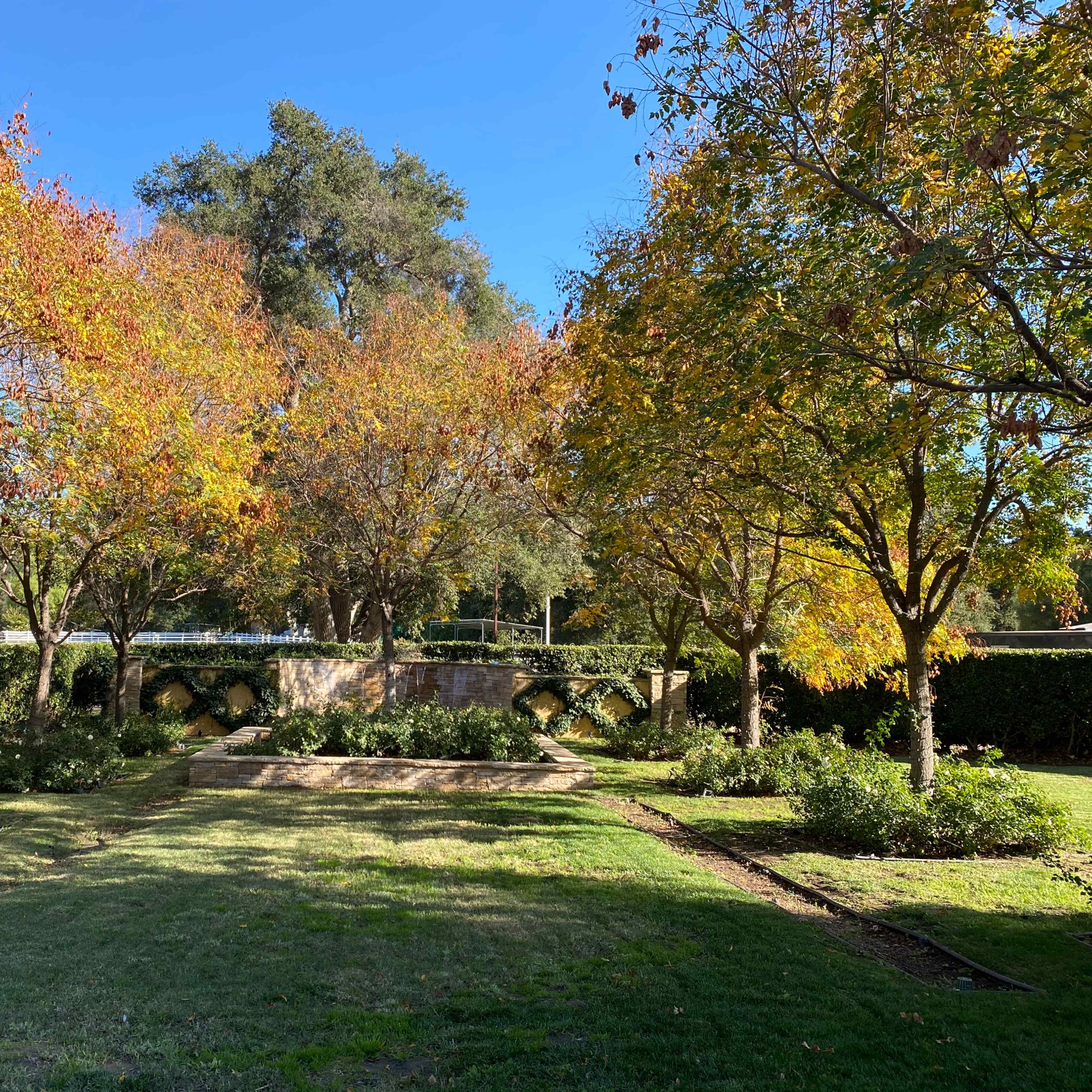 A landscaped area features several trees with autumn leaves and a stone bridge in the background.